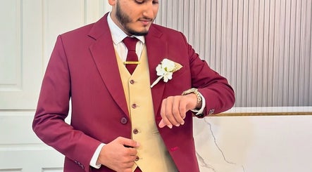 Person in burgundy suit with flower pin at Gloss Salon, Malé, Male, MV checking watch.