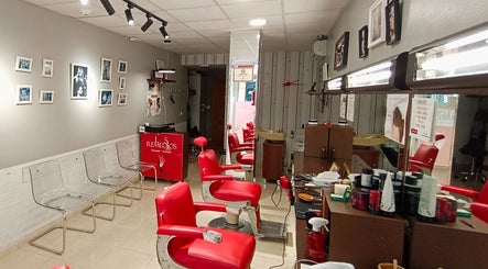 Interior moderno de Peluquería De Hombre Y Niños Los Remedios en Sevilla, Andalucía, ES con asientos rojos.