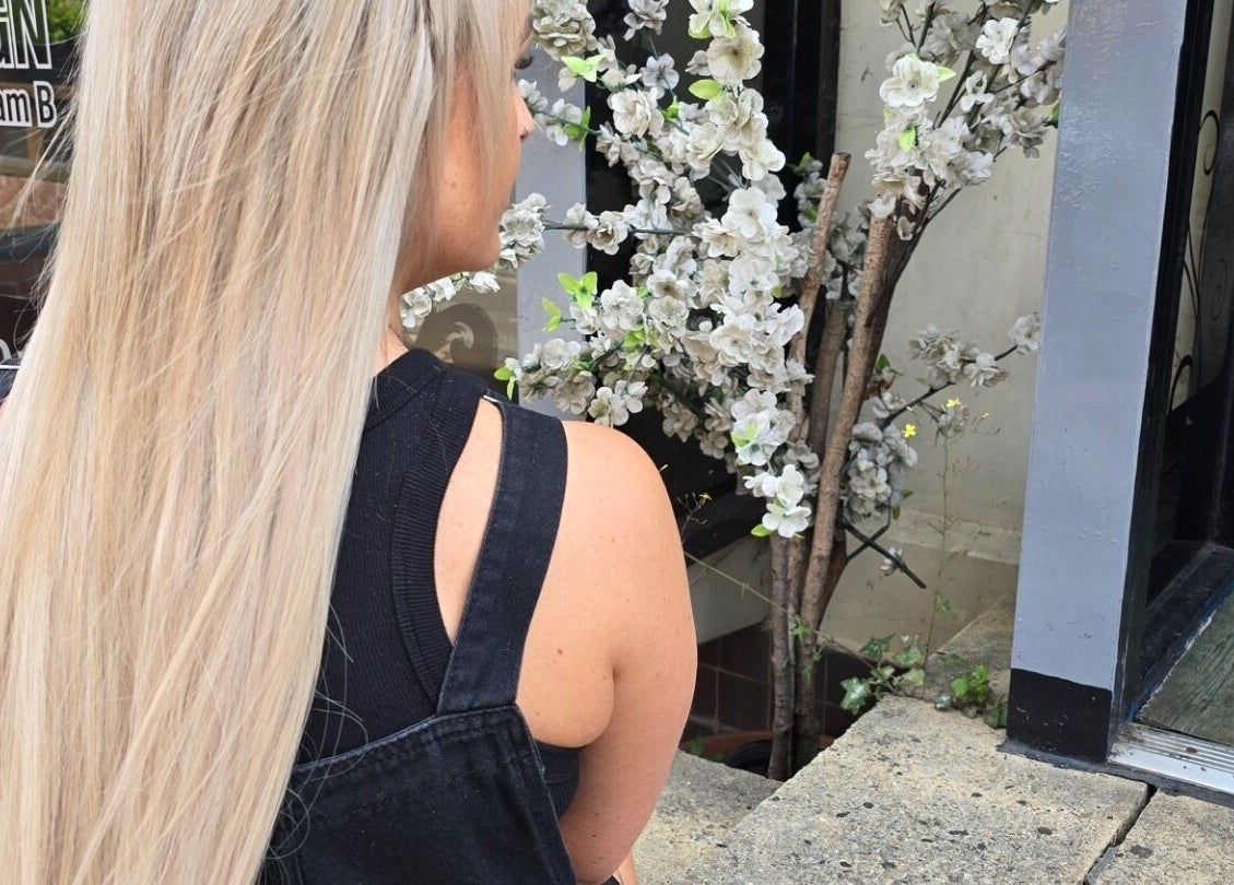 Blonde woman outside Alice Woolf salon, near white blossoms in Gloucester, England, GB.