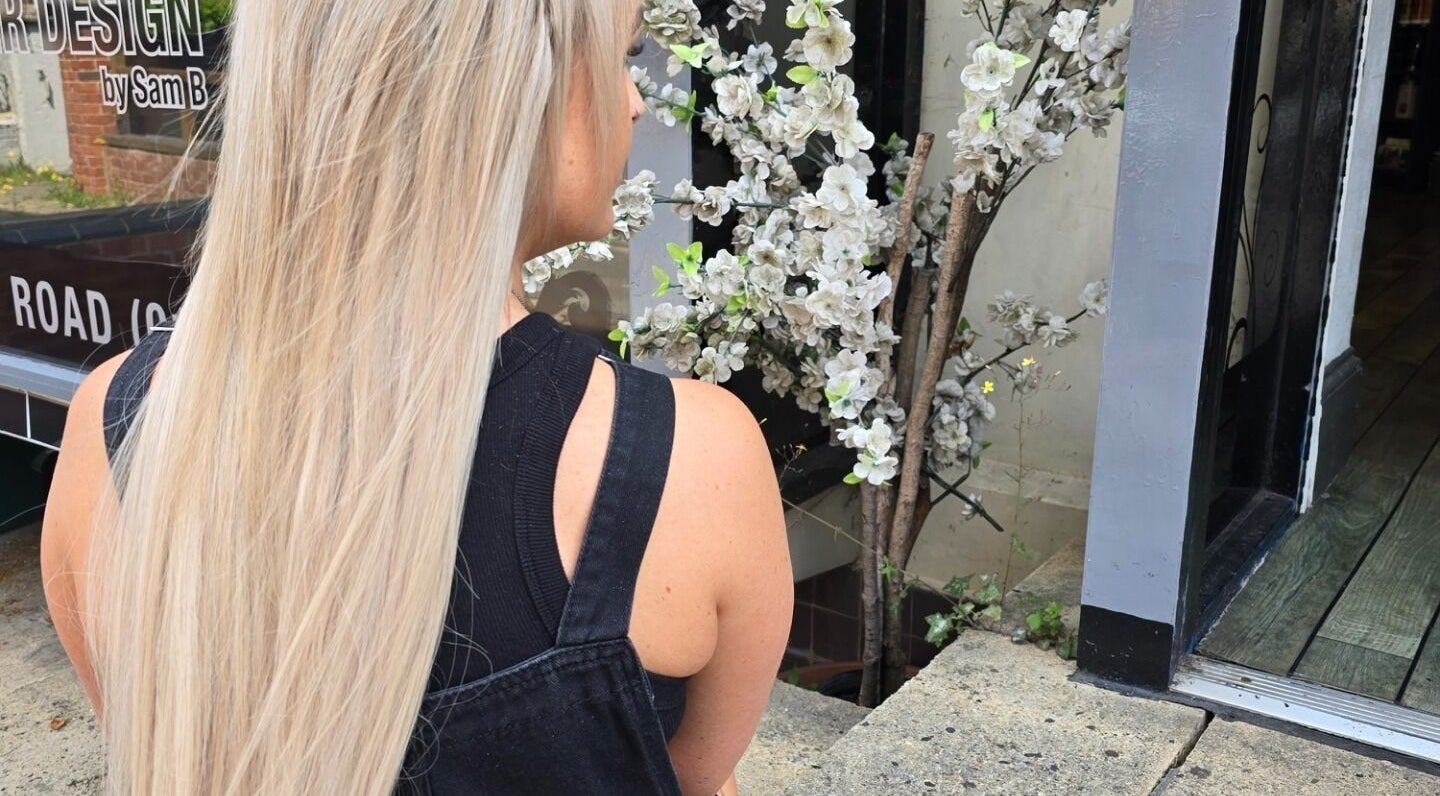 Blonde woman outside Alice Woolf salon, near white blossoms in Gloucester, England, GB.