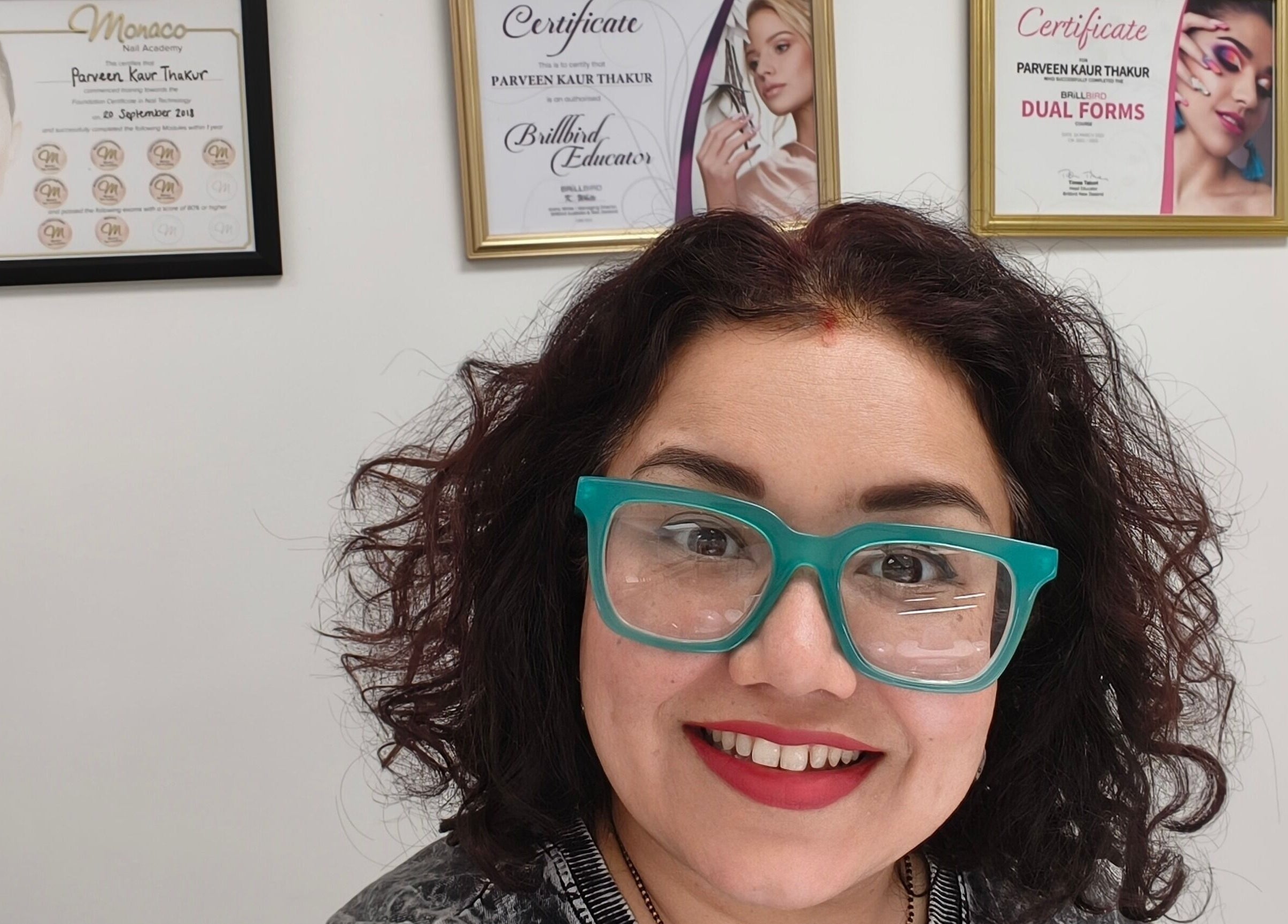 Smiling woman with stylish glasses at Goddess Nail Studio, Auckland, Auckland, NZ, showcasing certificates.