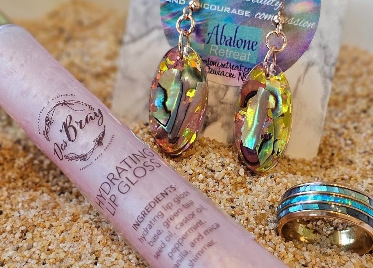 Abalone jewelry and lip gloss displayed on sand at Abalone Retreat in Stewiacke, Nova Scotia, CA.