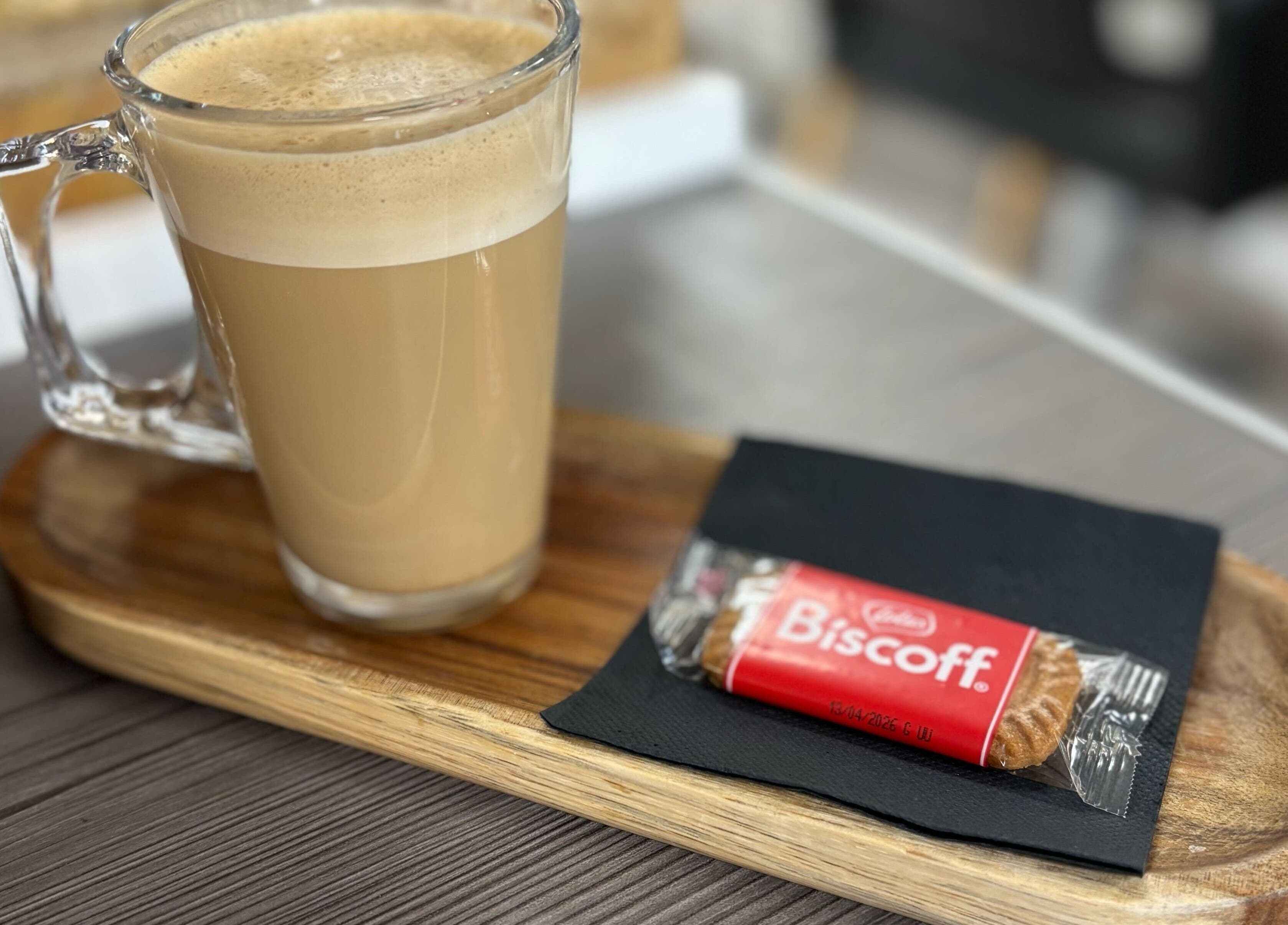 Glass latte with biscuit on a wooden tray at Clip’so Ely, Ely, England, GB. Cozy atmosphere.