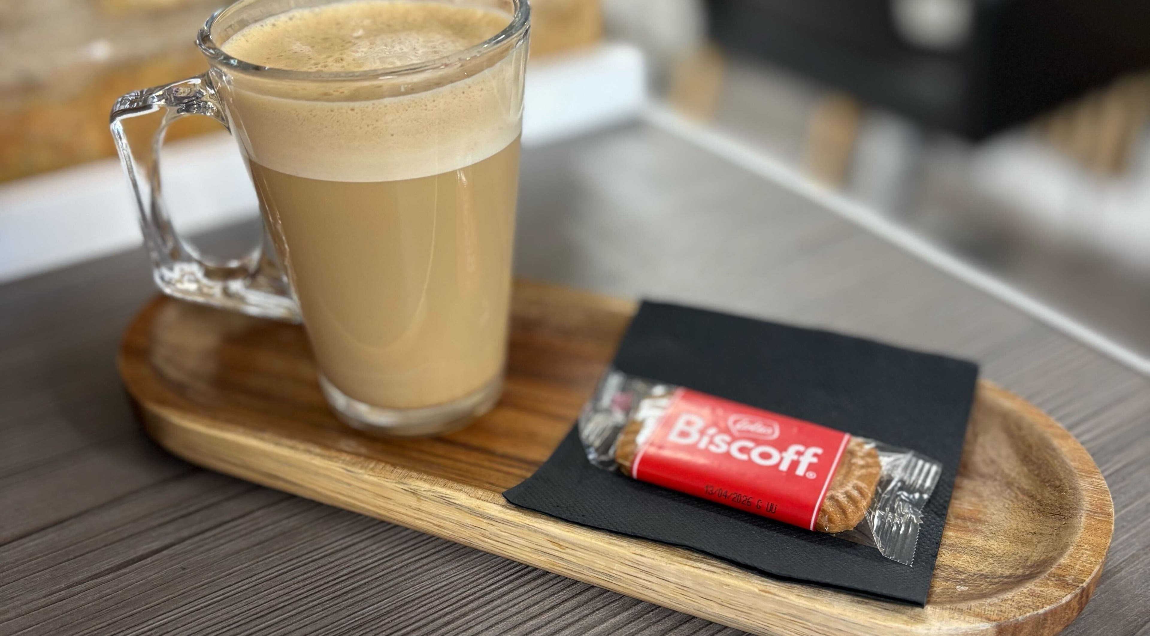 Glass latte with biscuit on a wooden tray at Clip’so Ely, Ely, England, GB. Cozy atmosphere.