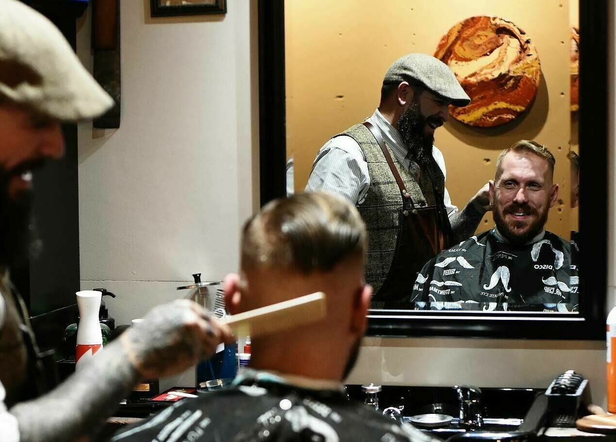 Barber styling a customer's hair at Two-Bit Barber Company in Sedalia, Missouri, US. Rustic interior mirror view.