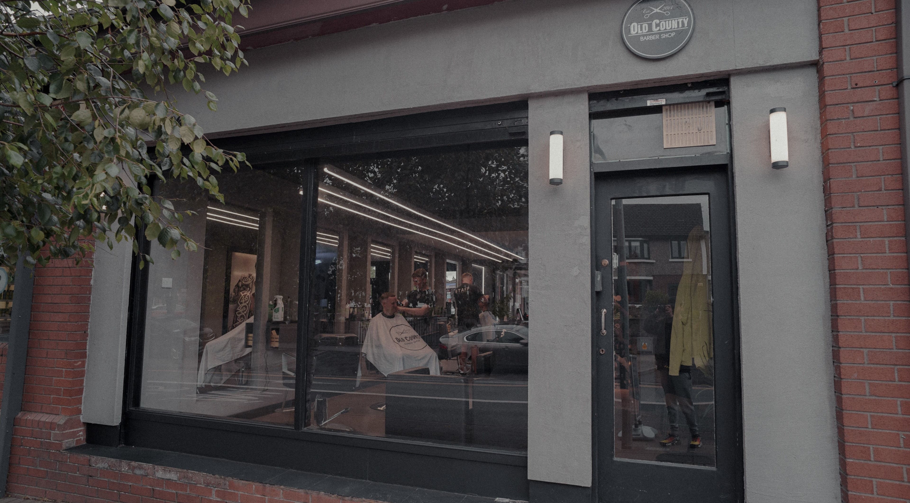 Exterior view of Old County Clondalkin barbershop in Dublin, County Dublin, IE, with customers inside.