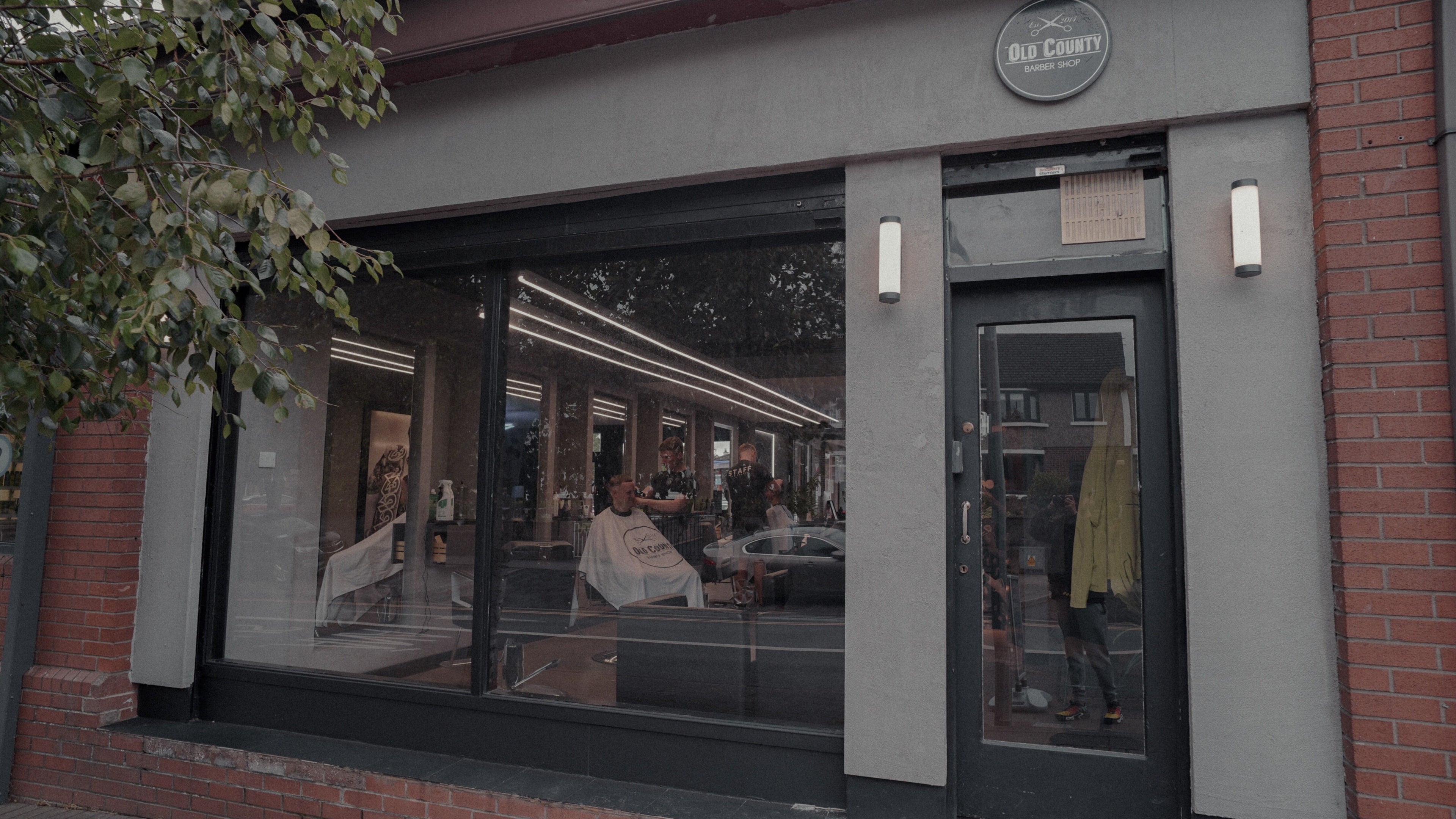 Exterior view of Old County Clondalkin barbershop in Dublin, County Dublin, IE, with customers inside.