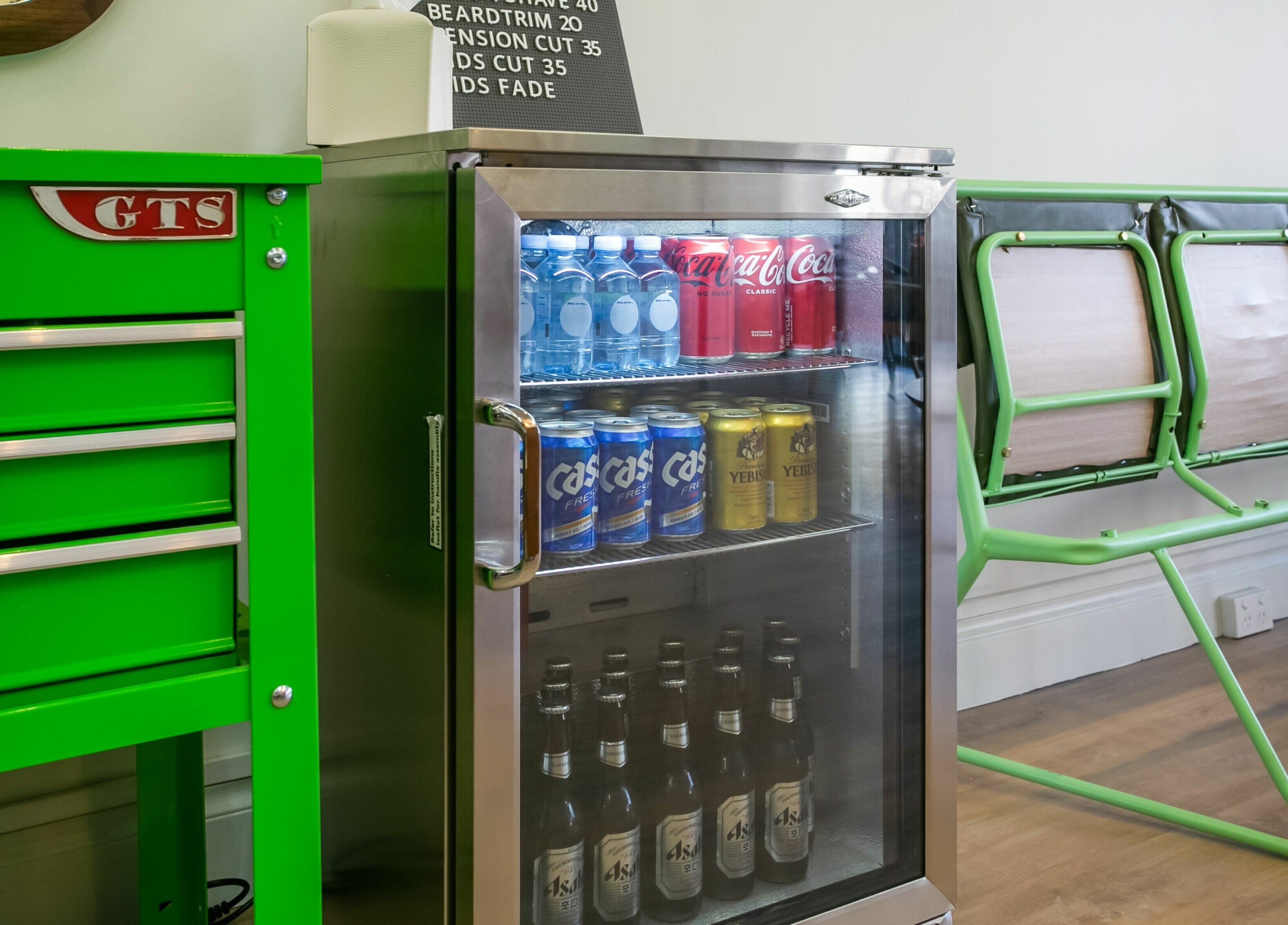 Chilled drinks in fridge at Daniel’s Barbershop, Melbourne, Victoria, AU. Green tool chest and seating nearby.