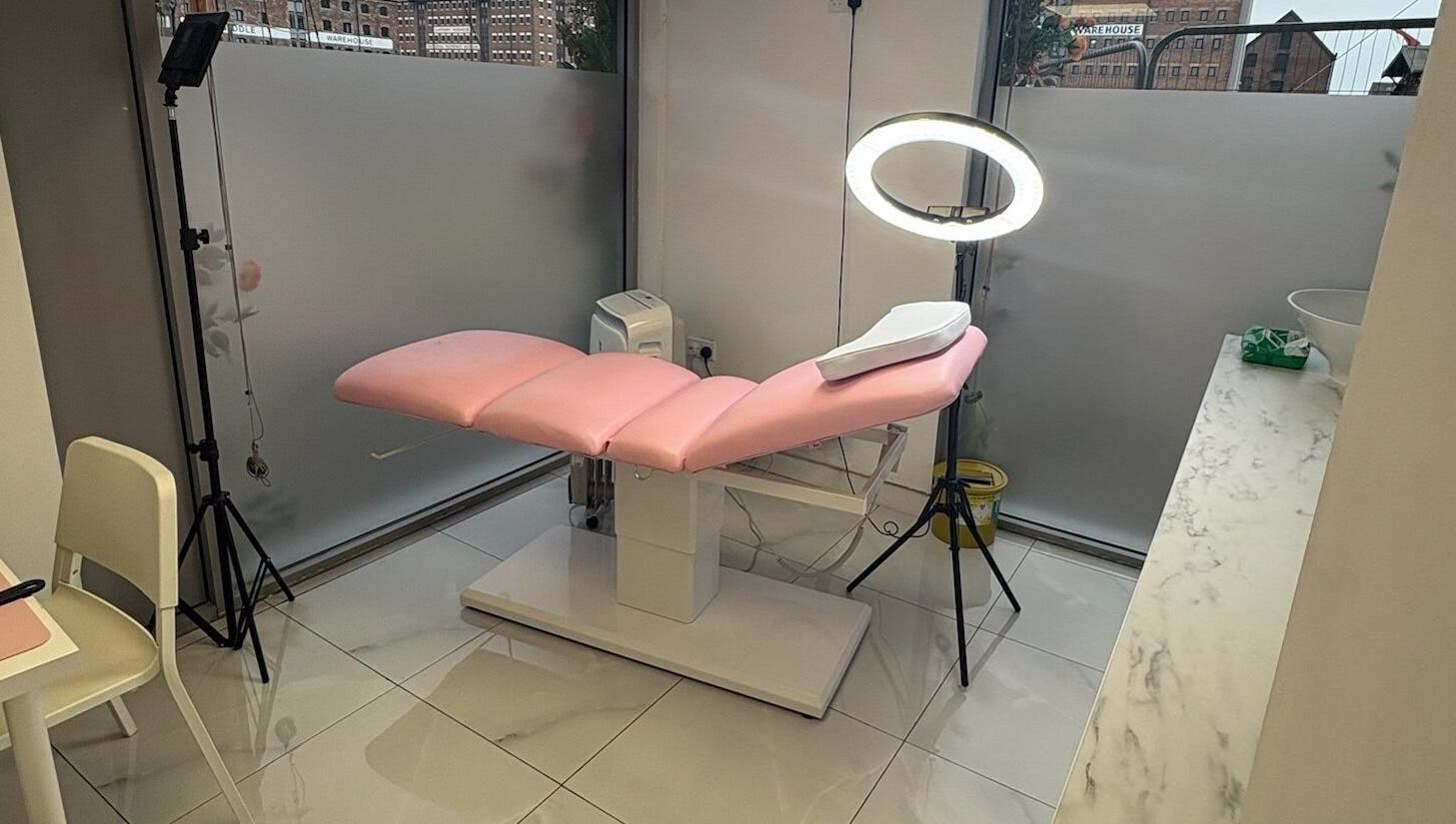 Sleek treatment room at Abbie Doctor Aesthetics, Gloucester, England. Features chic pink chair and modern lighting.