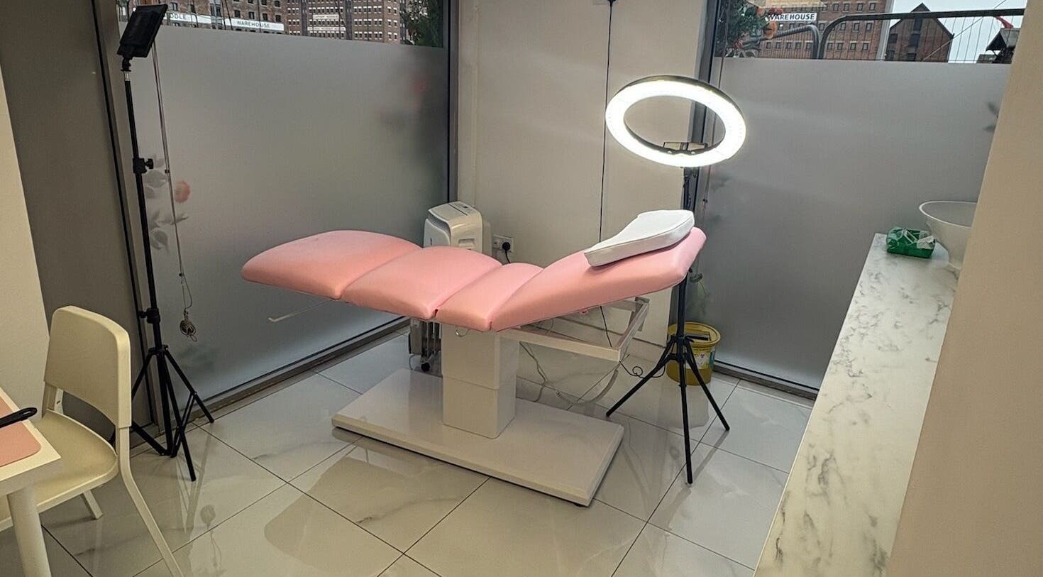 Sleek treatment room at Abbie Doctor Aesthetics, Gloucester, England. Features chic pink chair and modern lighting.