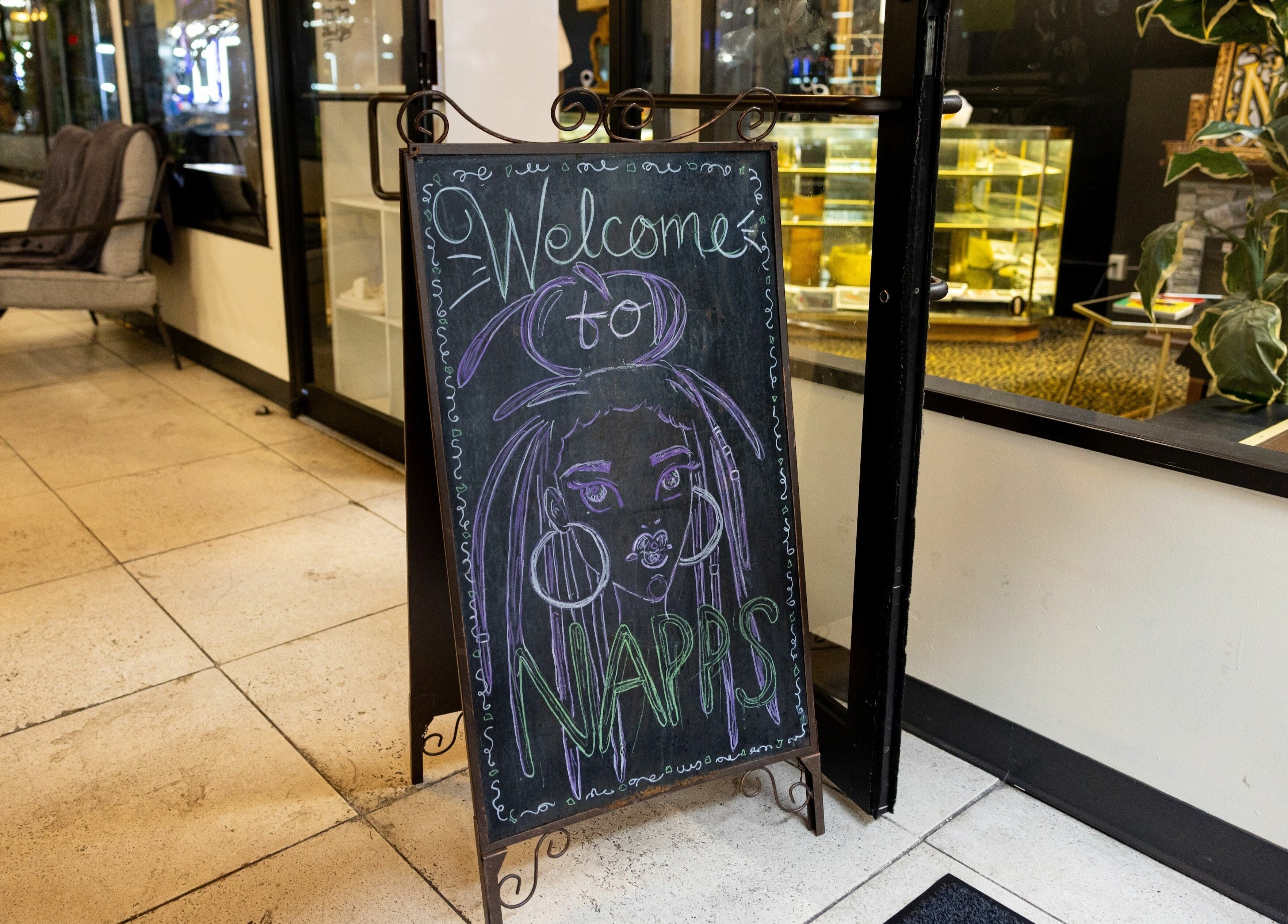Chalkboard sign welcomes guests to Napps Natural Hair Salon in St. Louis, Missouri, US with vibrant artwork.
