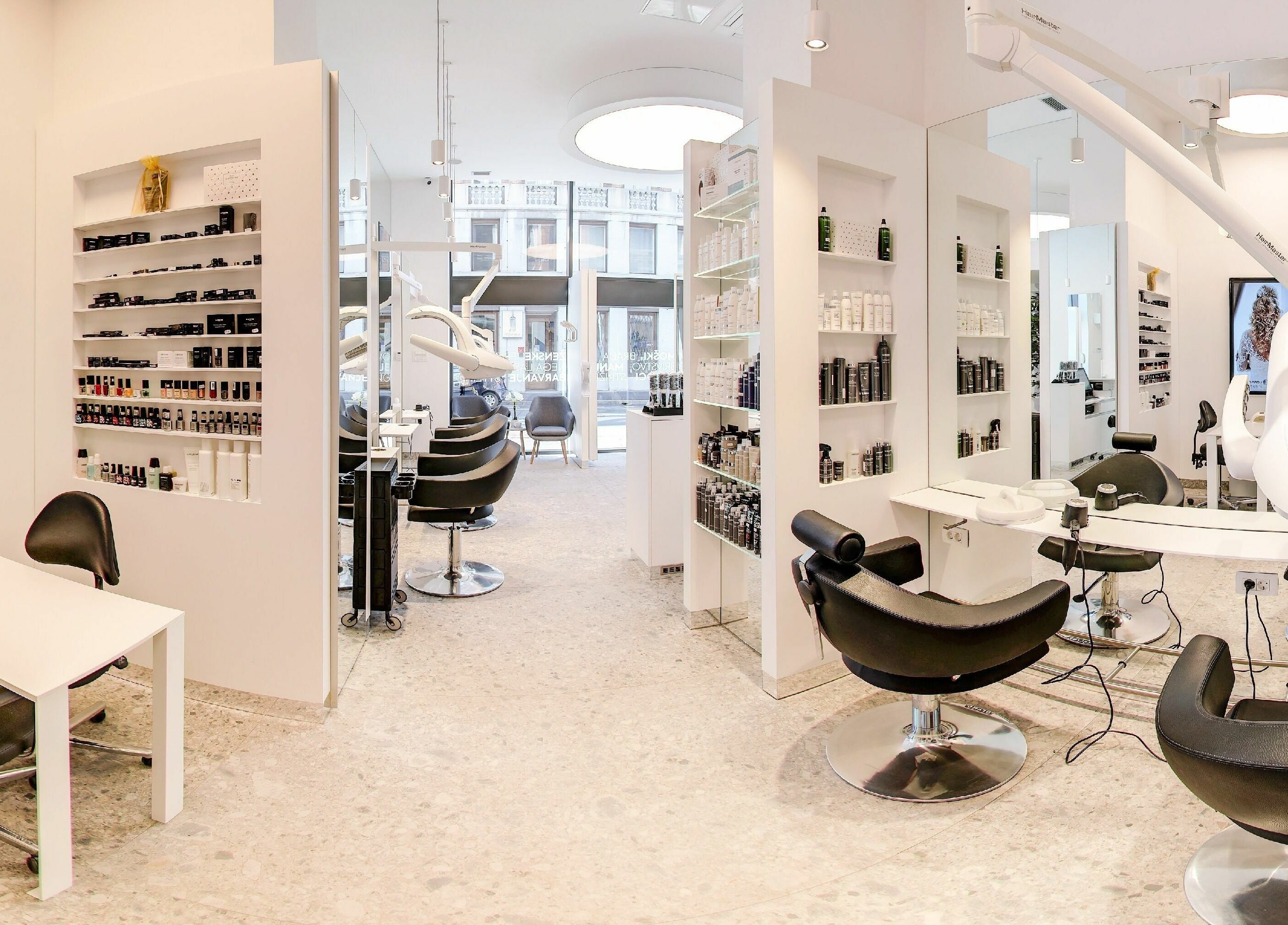 Sodobna notranjost Lassana Frizerski Salon - Miklošičeva 40, Ljubljana. Svetel prostor s stiliškimi stoli in izdelki.