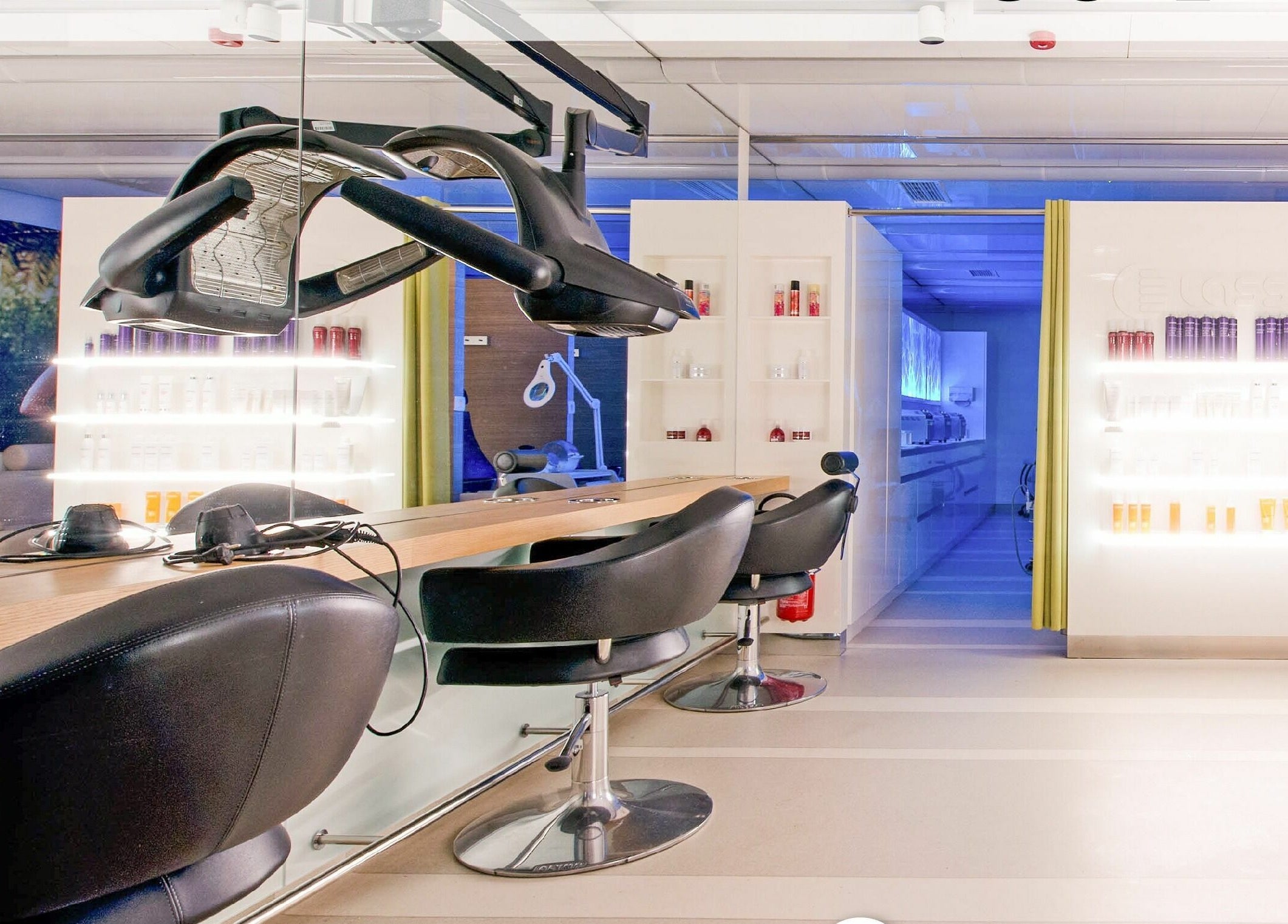 Notranjost Lassana Frizerski in Kozmetični Salon - Zaloška 7, Ljubljana, z modernimi stoli in osvetljenimi policami.