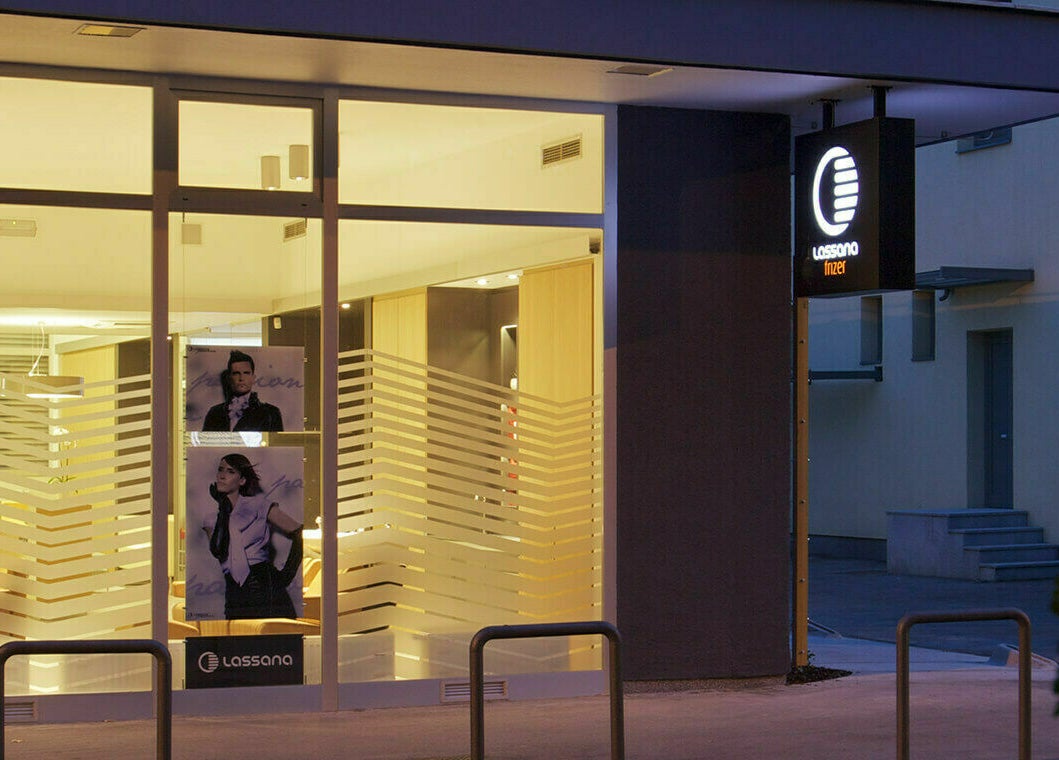 Večerni pogled na Lassana Frizerski Salon - Derčeva 31, Ljubljana, Ljubljana, SI, osvetljen z elegantno dekoracijo.