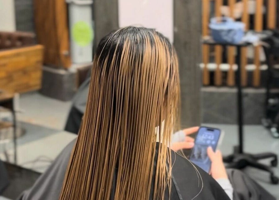 Client at Vsalon in Vancouver, British Columbia, CA, with sleek, straightened hair viewing a phone.