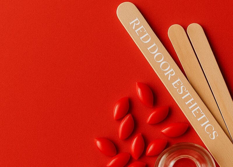 Red Door Esthetics branding with wooden tools in Leduc, Alberta, CA on vibrant red background.