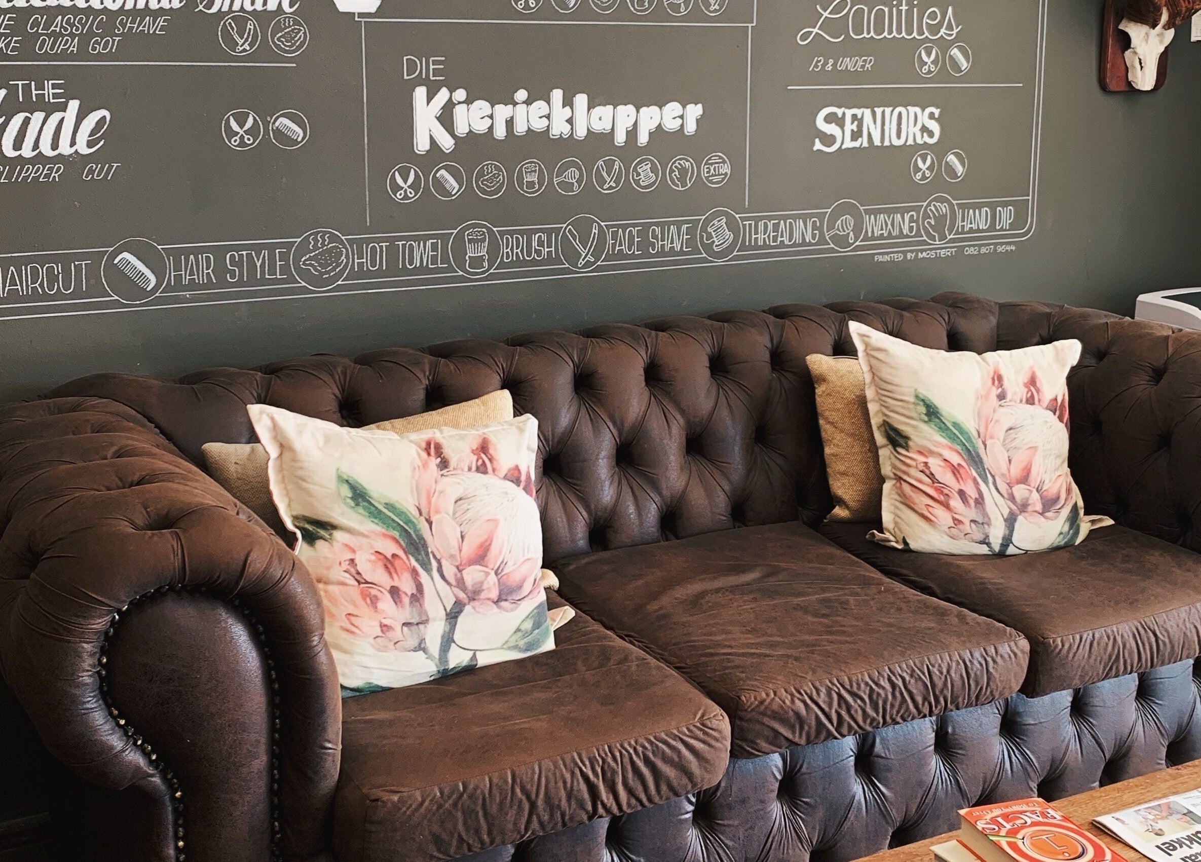 Cozy vintage couch at Kuif & Baard Barbershop, Pretoria, with chalkboard menu on the wall.