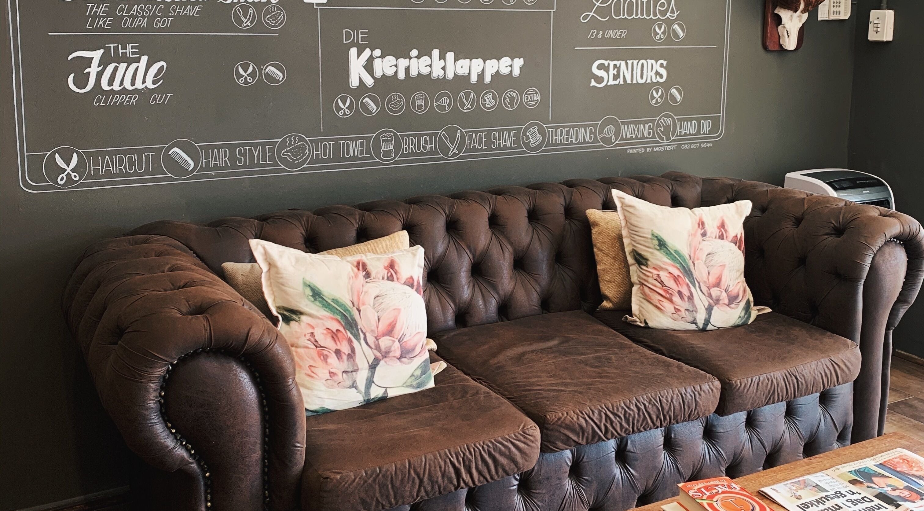 Cozy vintage couch at Kuif & Baard Barbershop, Pretoria, with chalkboard menu on the wall.