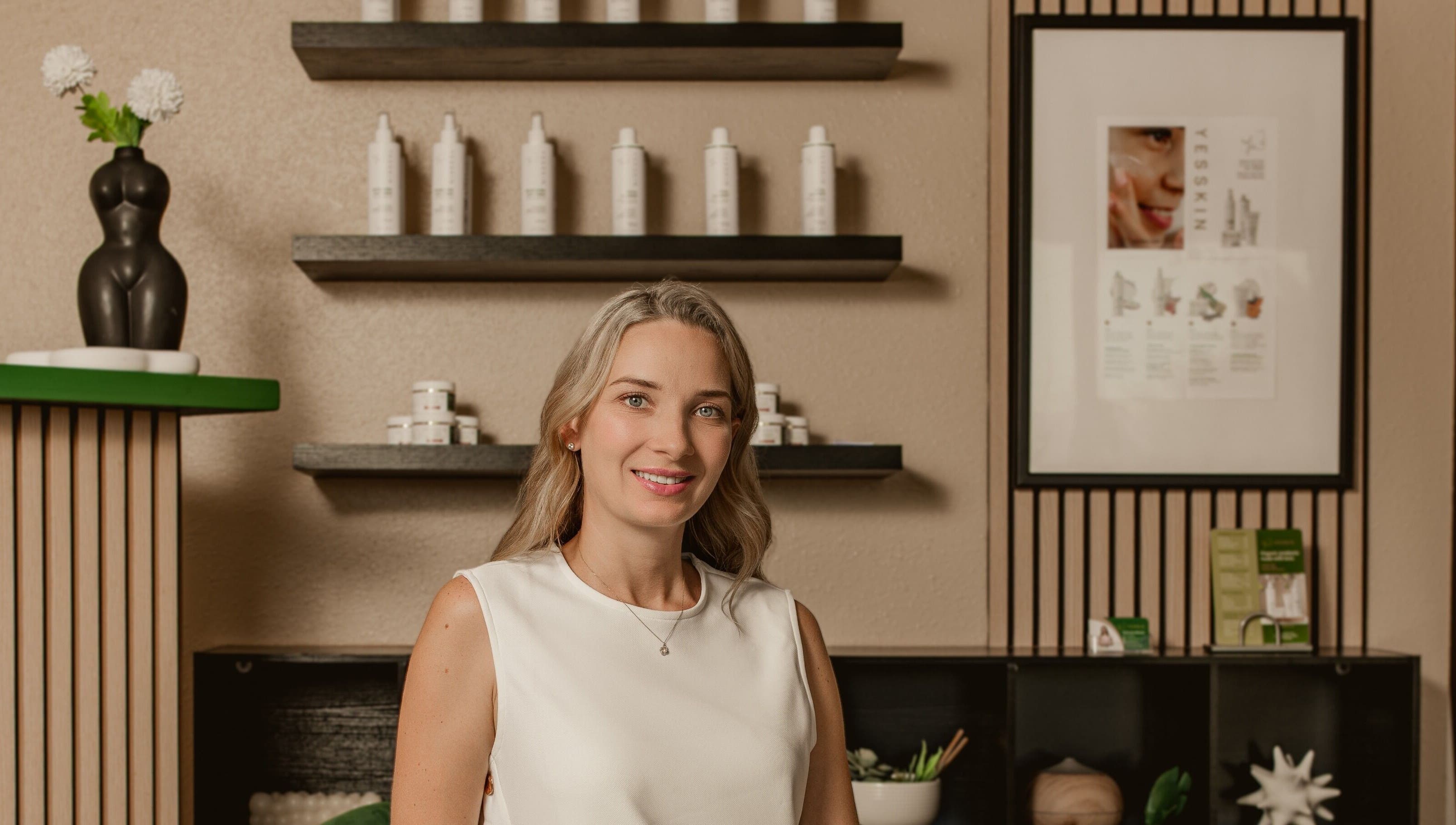 Smiling professional at Yesskin Skin Care, Tarpon Springs, Florida, US with product shelves.