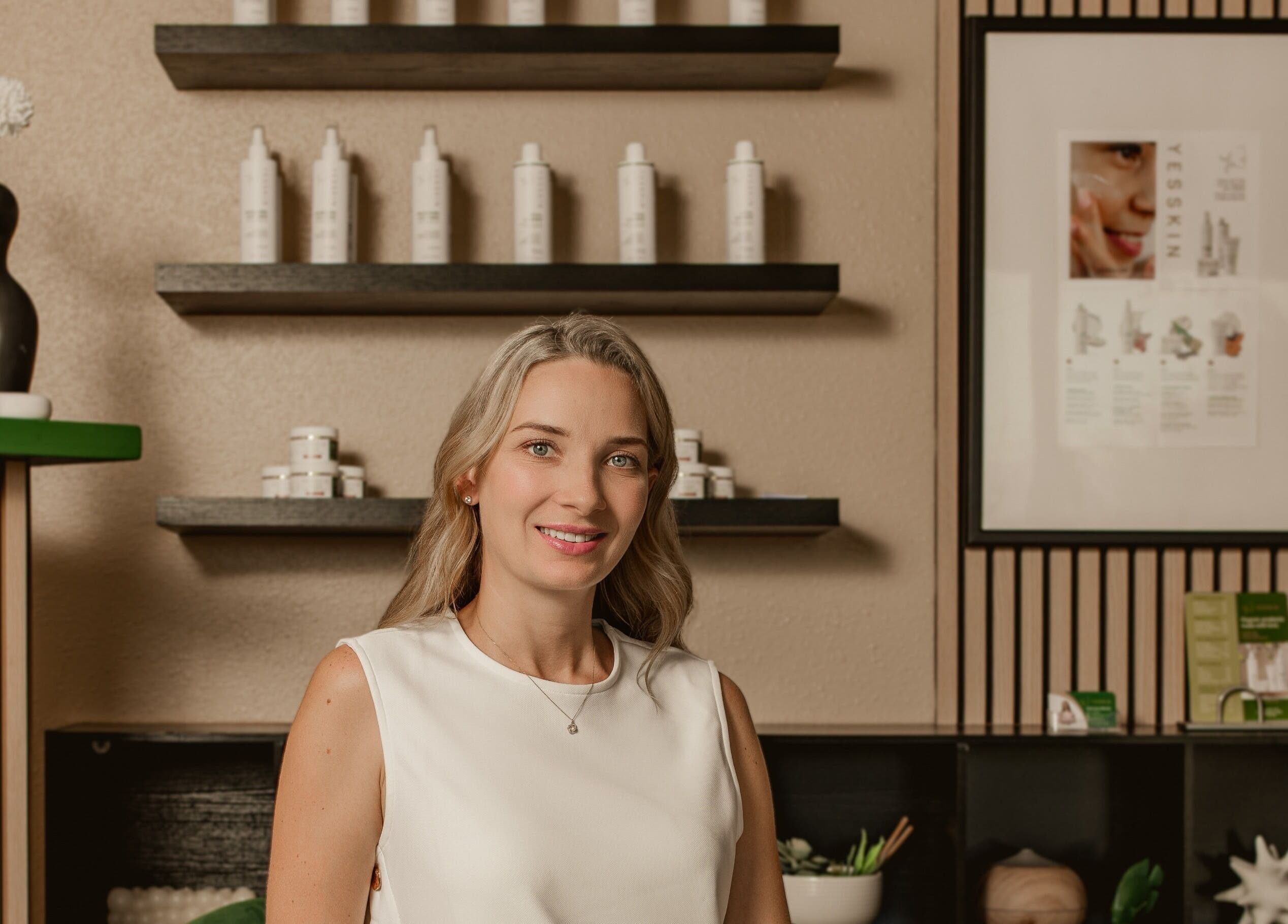 Smiling professional at Yesskin Skin Care, Tarpon Springs, Florida, US with product shelves.