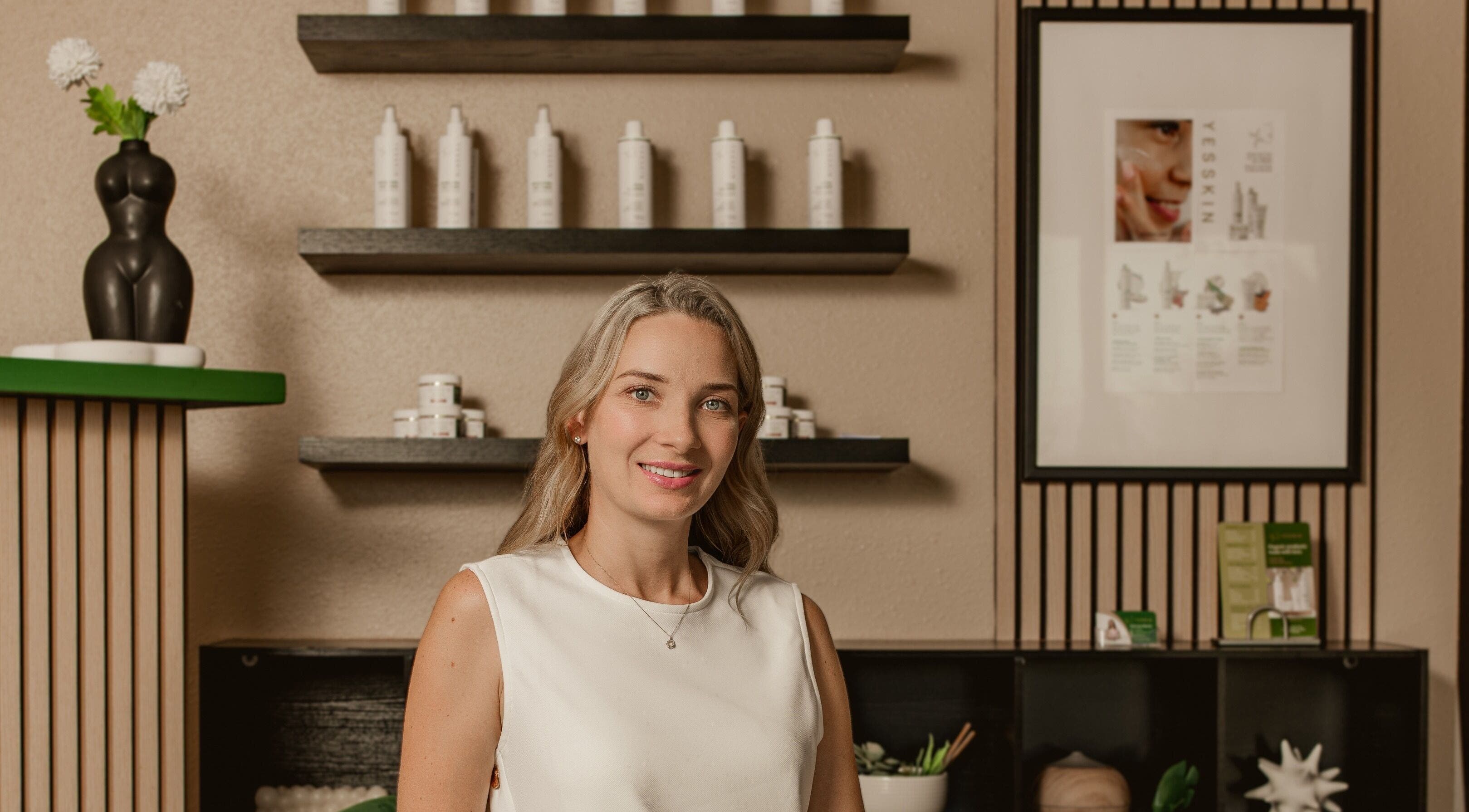 Smiling professional at Yesskin Skin Care, Tarpon Springs, Florida, US with product shelves.
