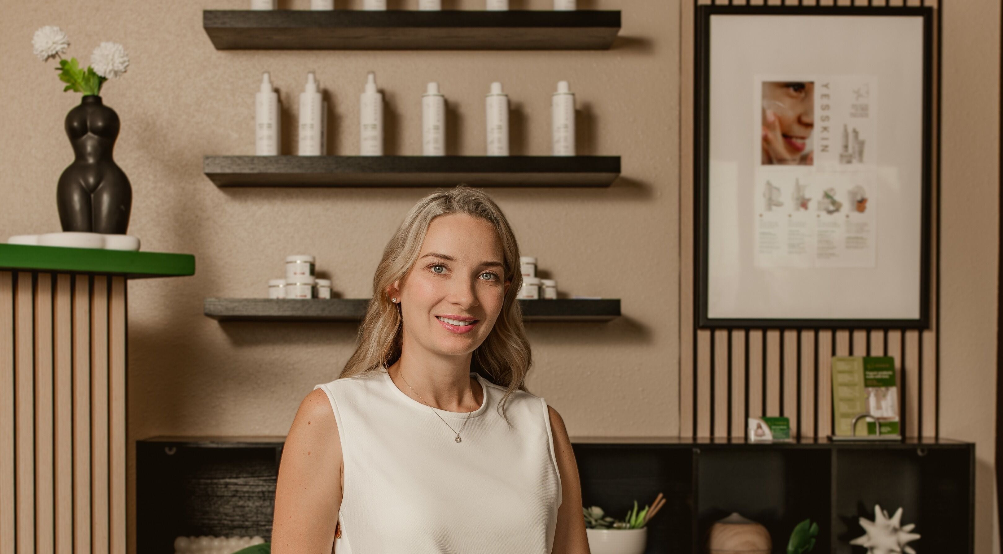 Smiling professional at Yesskin Skin Care, Tarpon Springs, Florida, US with product shelves.