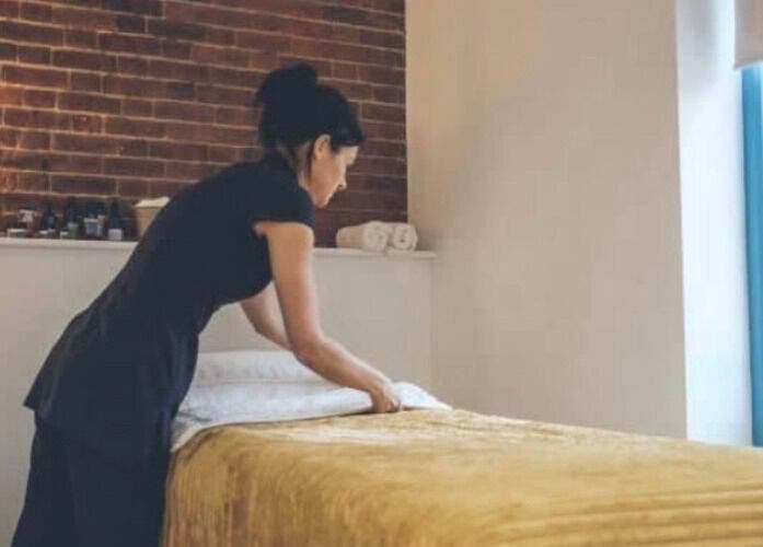 Therapist preparing a treatment room at The Barn Beauty Rooms, Norwich, England, GB, with warm ambiance.