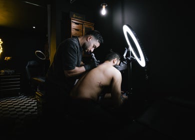 Tattoo artist working at BarberSmiths Tattoo Studio in London, England, GB with neon decor and professional setup.