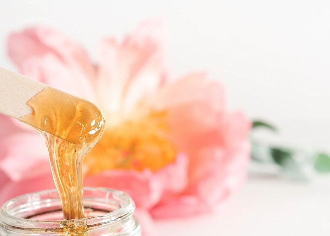 Warm wax in use at Illumine Skin and Wholeness Spa, Longmont, Colorado, US with pink floral backdrop.