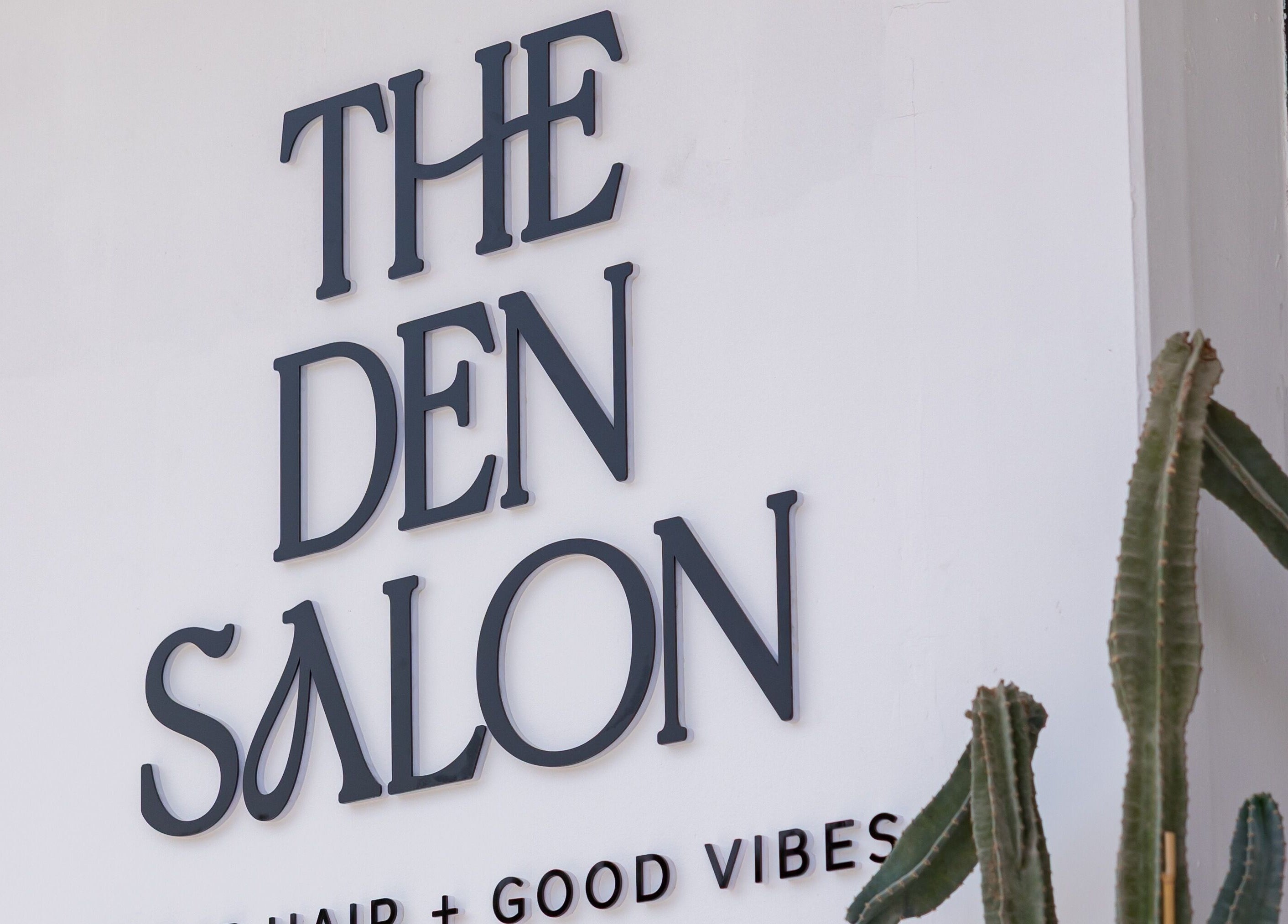Signage of The Den Salon in Dubai, AE, featuring bold lettering and a cactus plant.