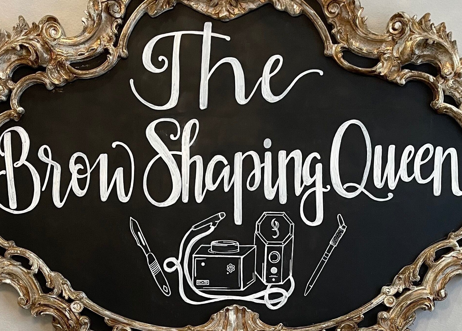 Elegant gold-framed sign for The Brow Shaping Queen in Frisco, Texas, US, showcasing beauty services.