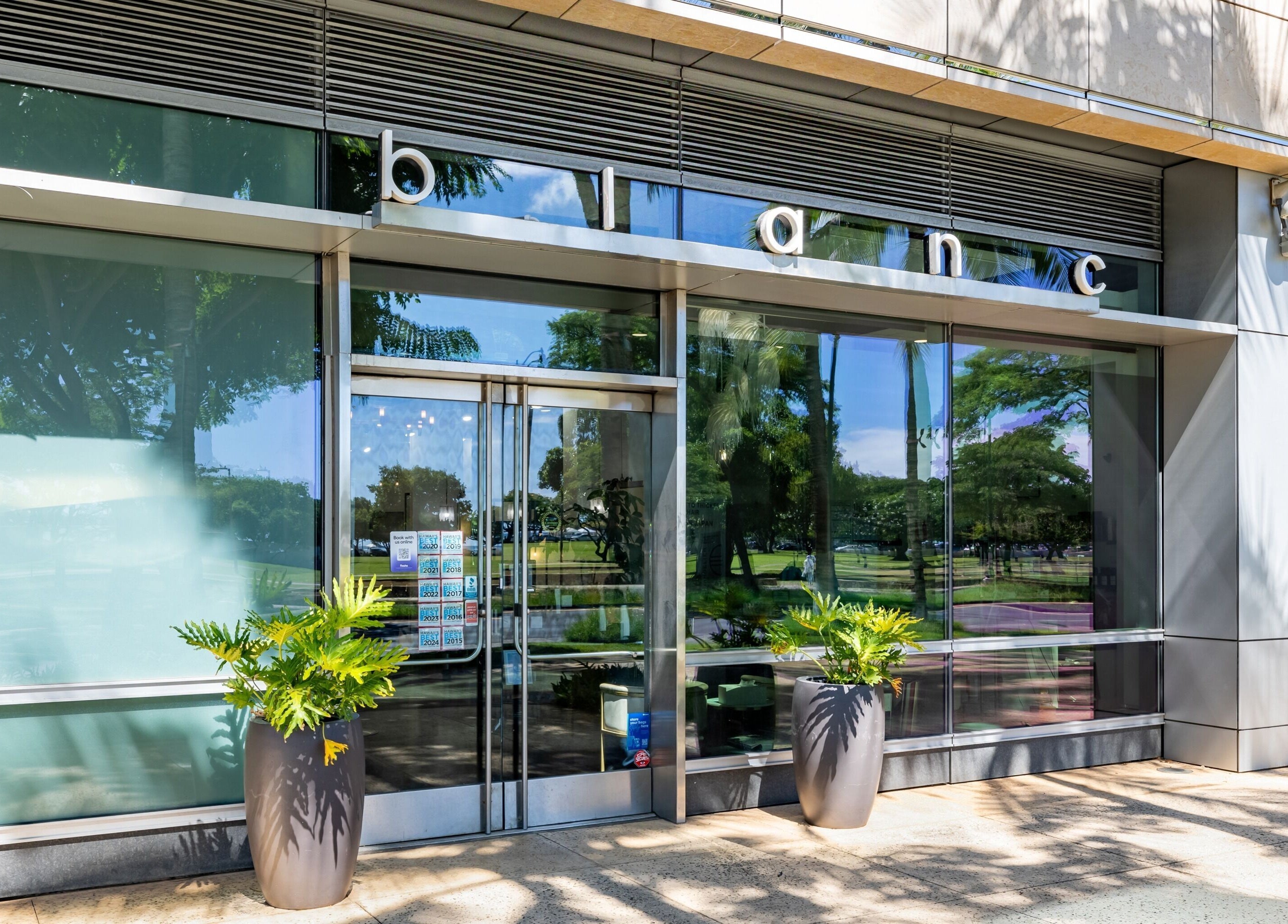 Entrance of Salon Blanc the celebrities salon in Honolulu, Hawaii, US, featuring glass doors and lush plants.