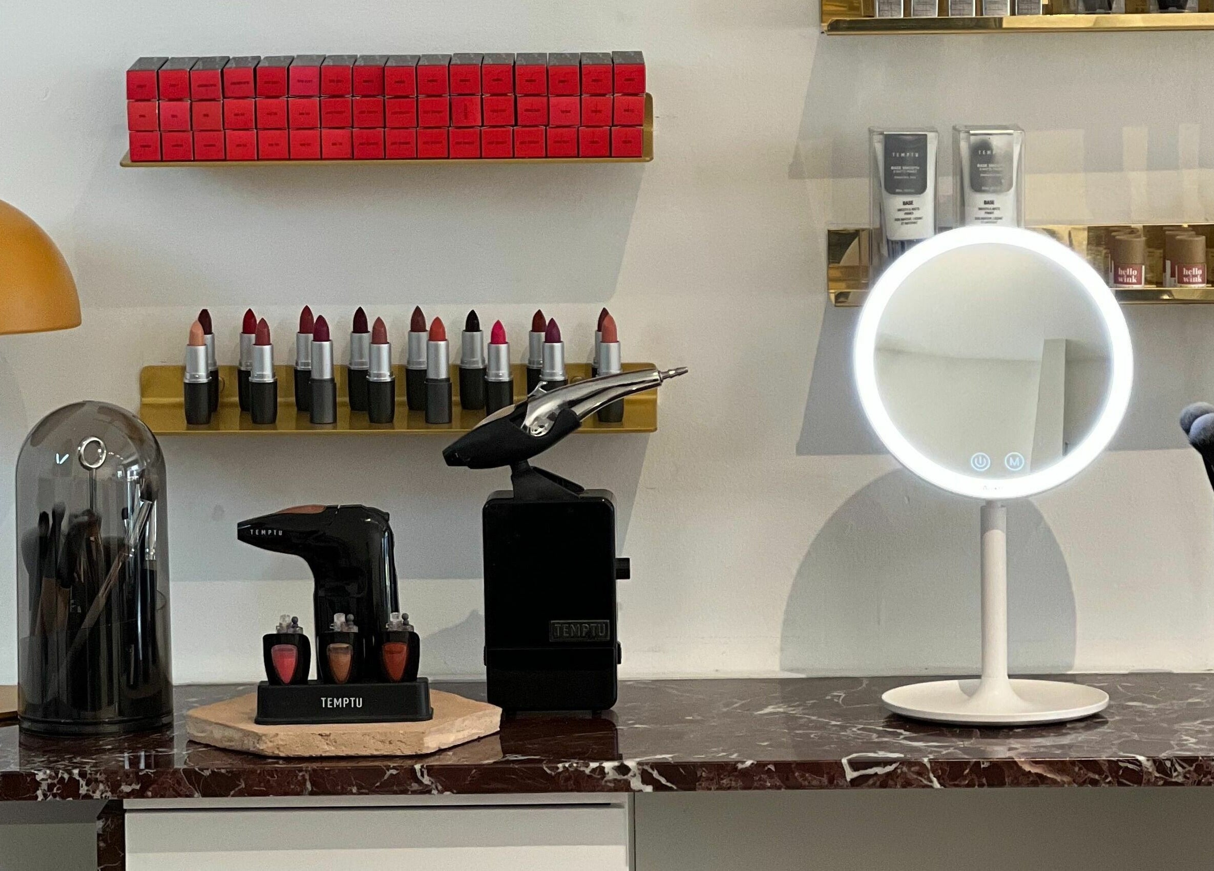 Makeup display at LittleLAB in Bath, England, GB, featuring lipsticks, brushes, and a lit mirror.