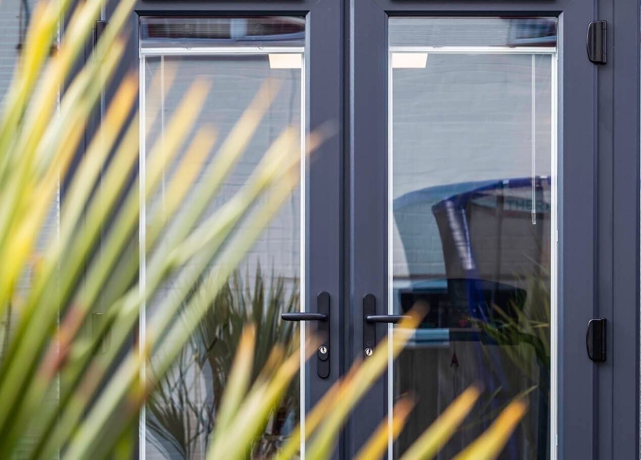 Inviting glass doors of MC Sports Therapy in Stevenage, England, GB with lush plant reflections.