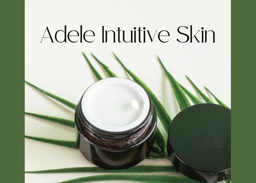 Adele Intuitive Skin Luton showcases a luxurious cream jar on lush green leaves.