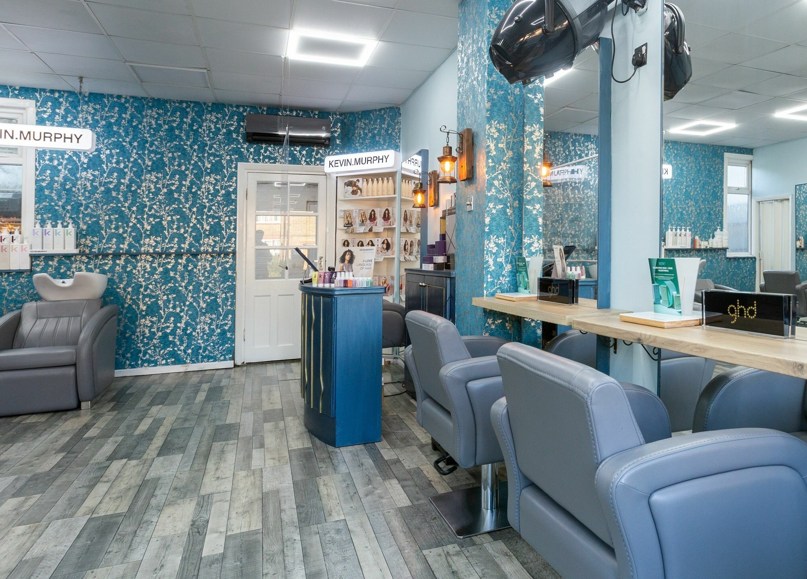 Modern salon interior at The Beauty Inn, London, England, GB with blue floral walls and stylish gray chairs.