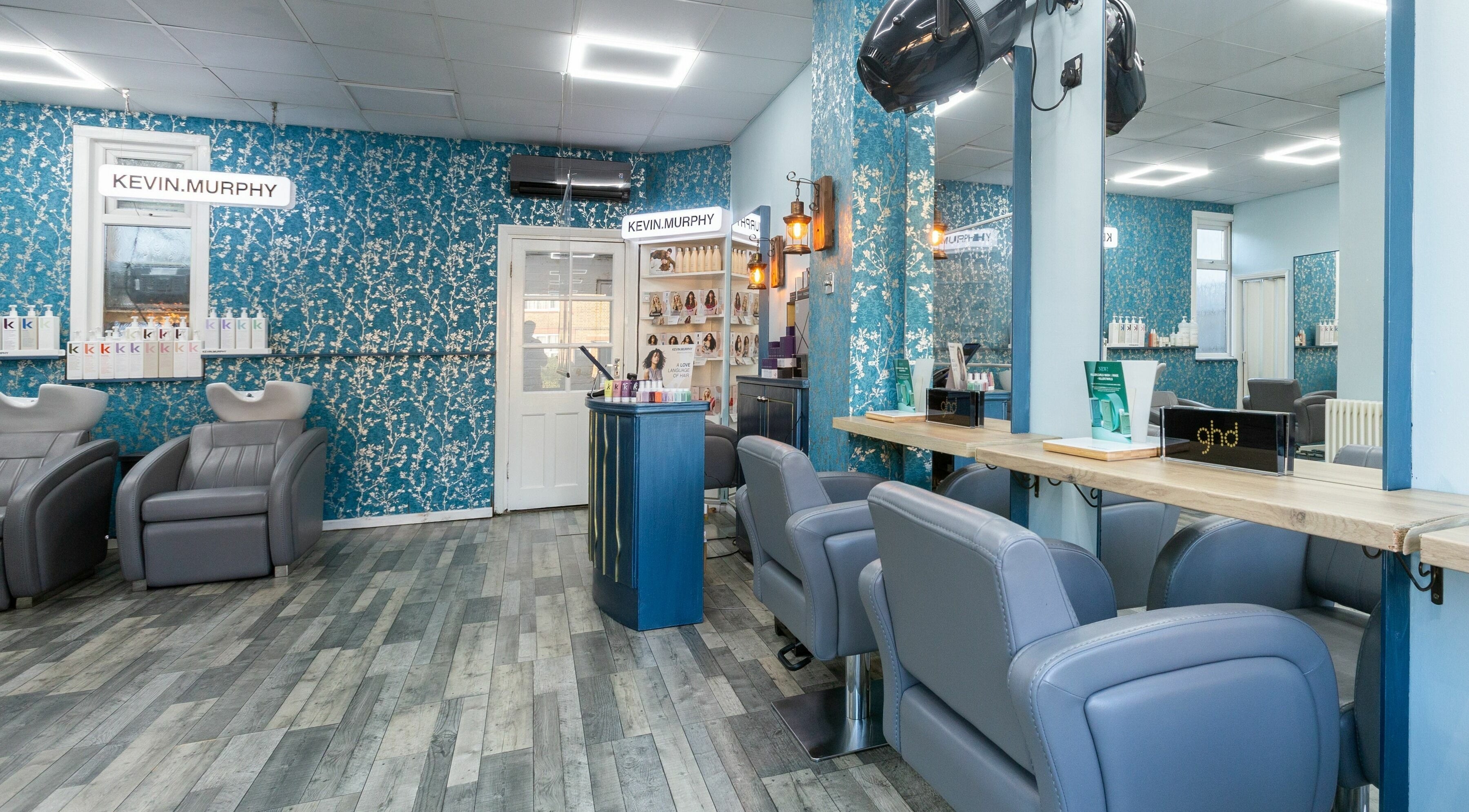 Modern salon interior at The Beauty Inn, London, England, GB with blue floral walls and stylish gray chairs.