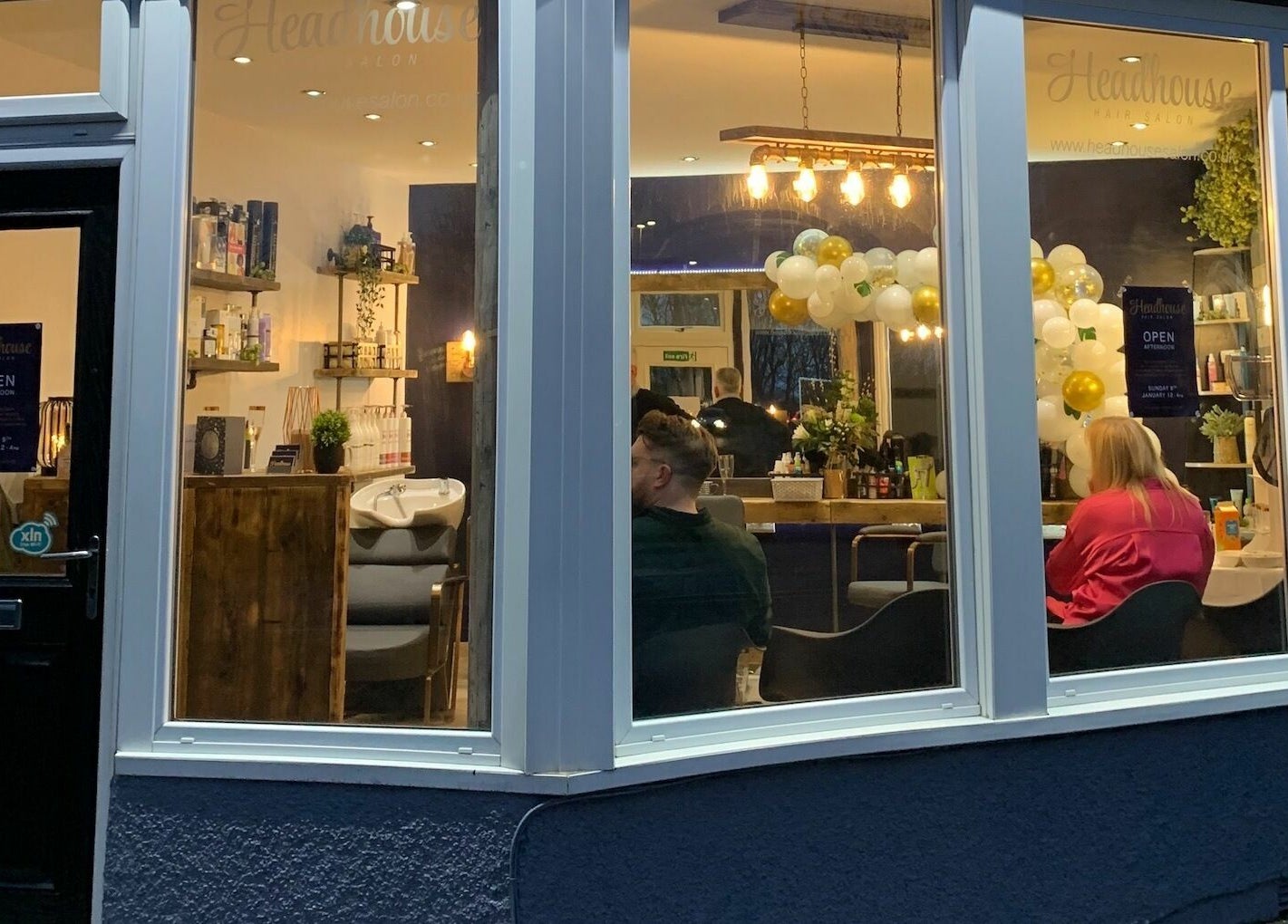 Headhouse salon interior with customers at Horsforth, England, GB, warmly lit through large windows.