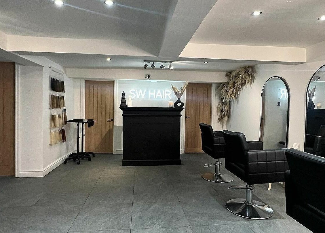 Modern interior of SW Hair Extensions salon in Watnall, England, GB featuring sleek black chairs and large mirrors.