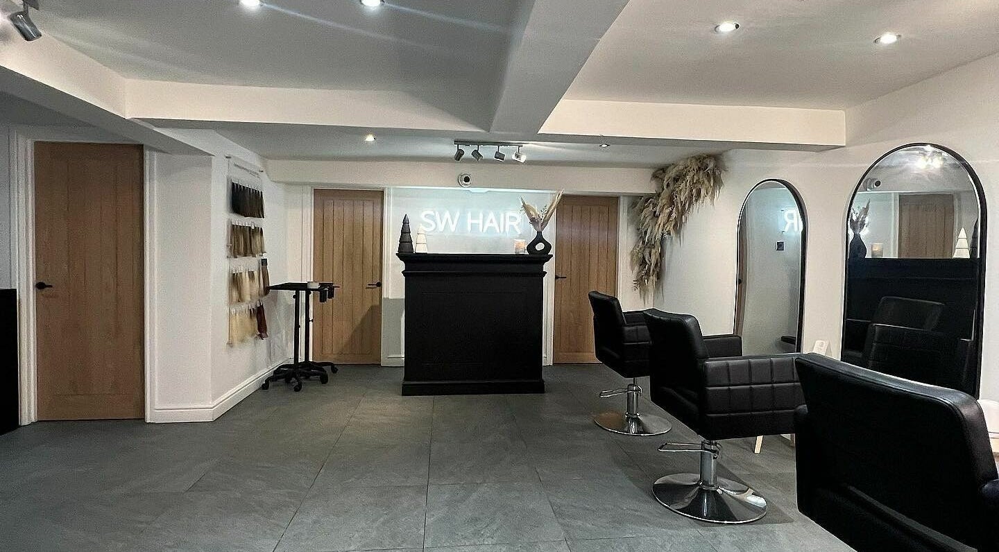 Modern interior of SW Hair Extensions salon in Watnall, England, GB featuring sleek black chairs and large mirrors.