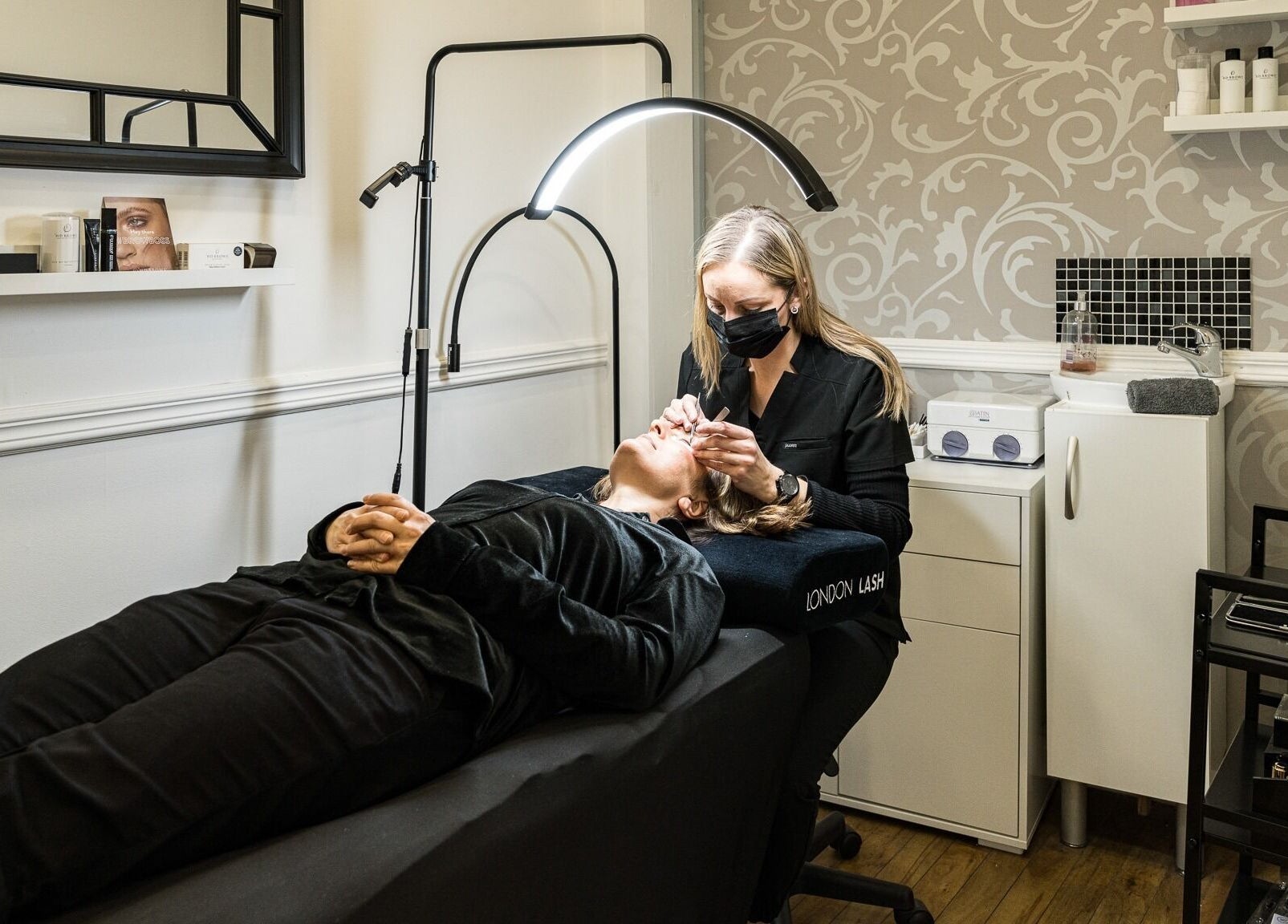 Aesthetician performs lash treatment at SB Studio in Coulsdon, England, GB in a serene, stylish space.