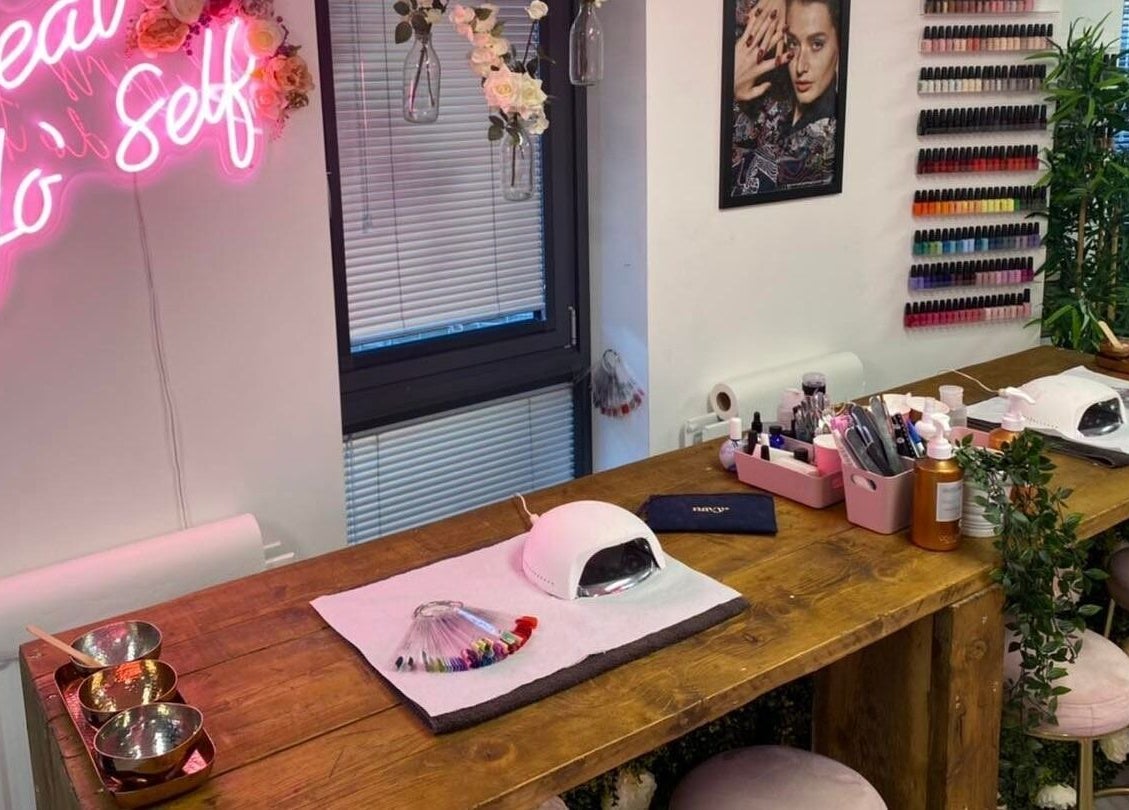 Stylish nail salon setup at The Beauty House, Bristol, England, GB featuring neon sign and colorful polish display.