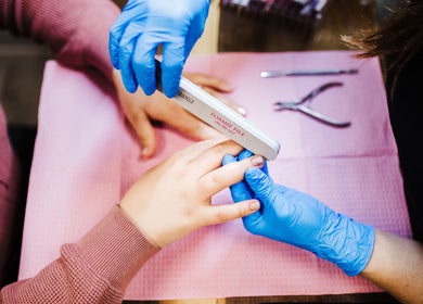 Professional manicure at Polished Designs by Danielle, Mount Horeb, Wisconsin, US. Blue-gloved hands filing nails.