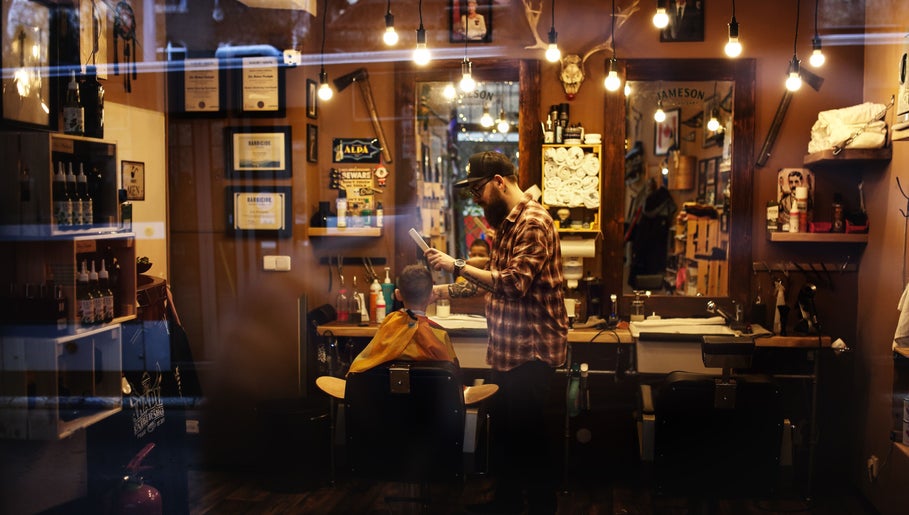 Interior of The Canadian Barbershop in Praha, CZ, showcasing a barber styling a customer's hair.