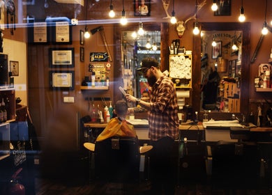 Interior of The Canadian Barbershop in Praha, CZ, showcasing a barber styling a customer's hair.