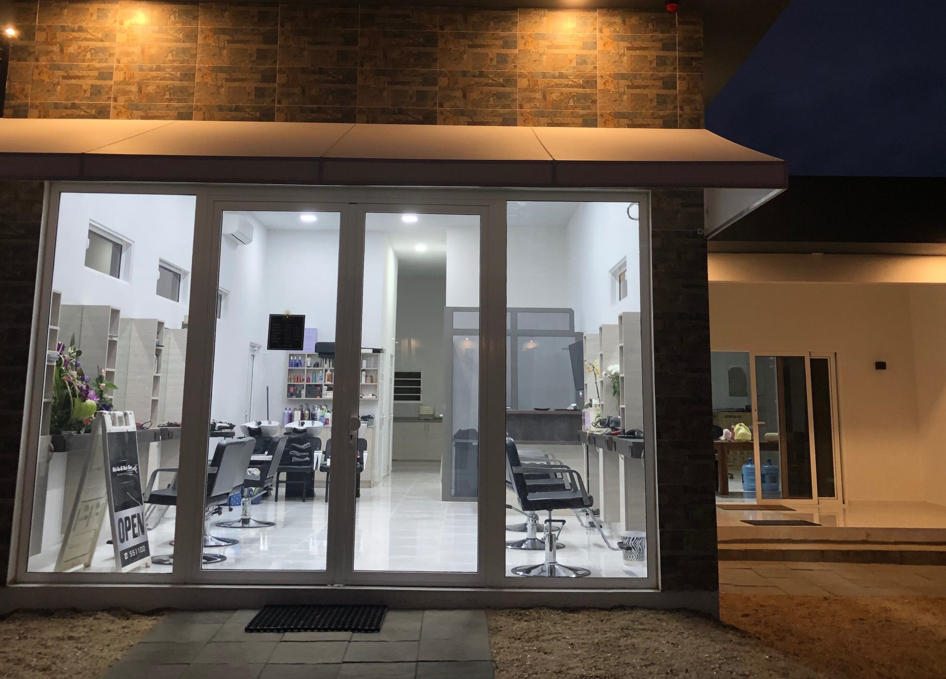 Night view of Mel An Gi Hair NV, a modern salon in Paramaribo, Paramaribo, SR with glass doors and stylish chairs.