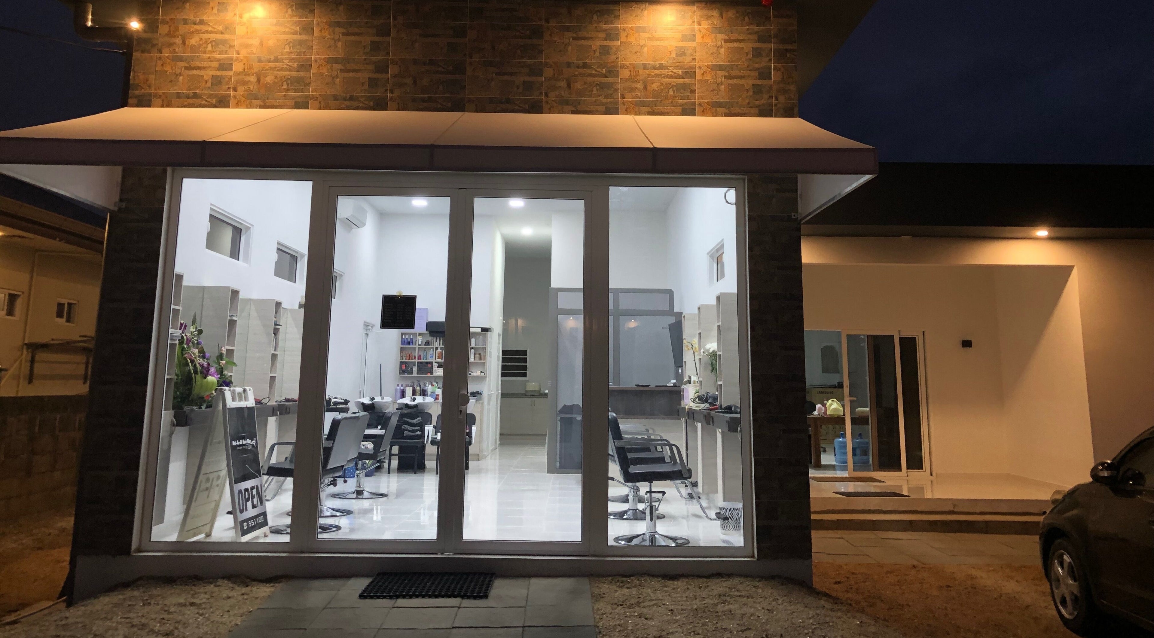 Night view of Mel An Gi Hair NV, a modern salon in Paramaribo, Paramaribo, SR with glass doors and stylish chairs.