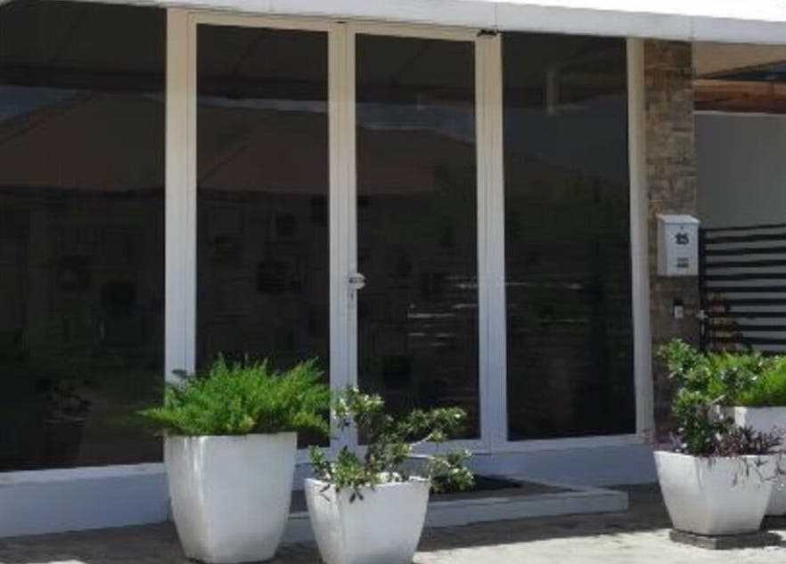 Front entrance of Mel An Gi Hair NV in Paramaribo, Paramaribo, SR with modern glass doors and lush greenery.