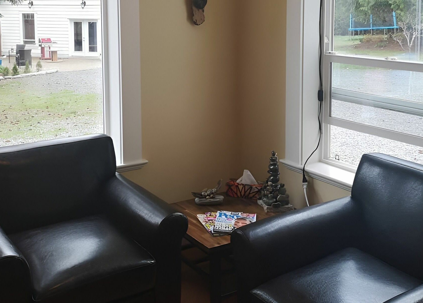 Inviting lounge area at Kat's Hair Studio, Sooke, British Columbia, CA. Two black chairs by bright windows.