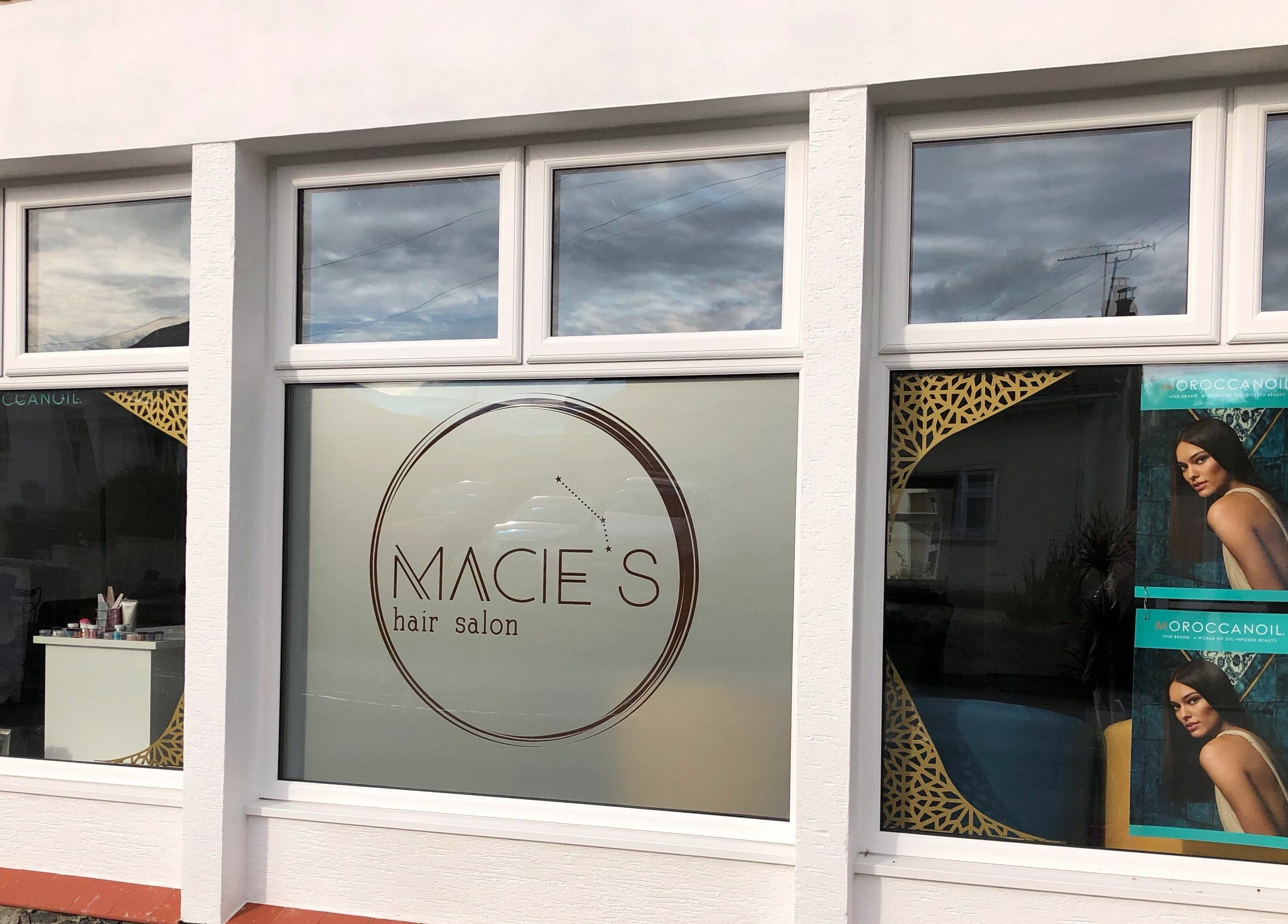 Front view of Macie's hair salon in Guernsey, Castel, GG, showcasing stylish branding and MoroccanOil posters.